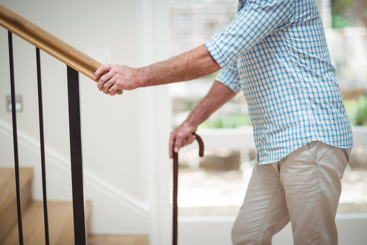 Mid section of senior man climbing upstairs with walking stick at home
