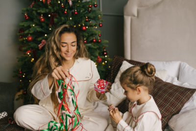 mother and daughter packing and wrapping presents in a cosy, decorated bedroom with a Christmas tree.