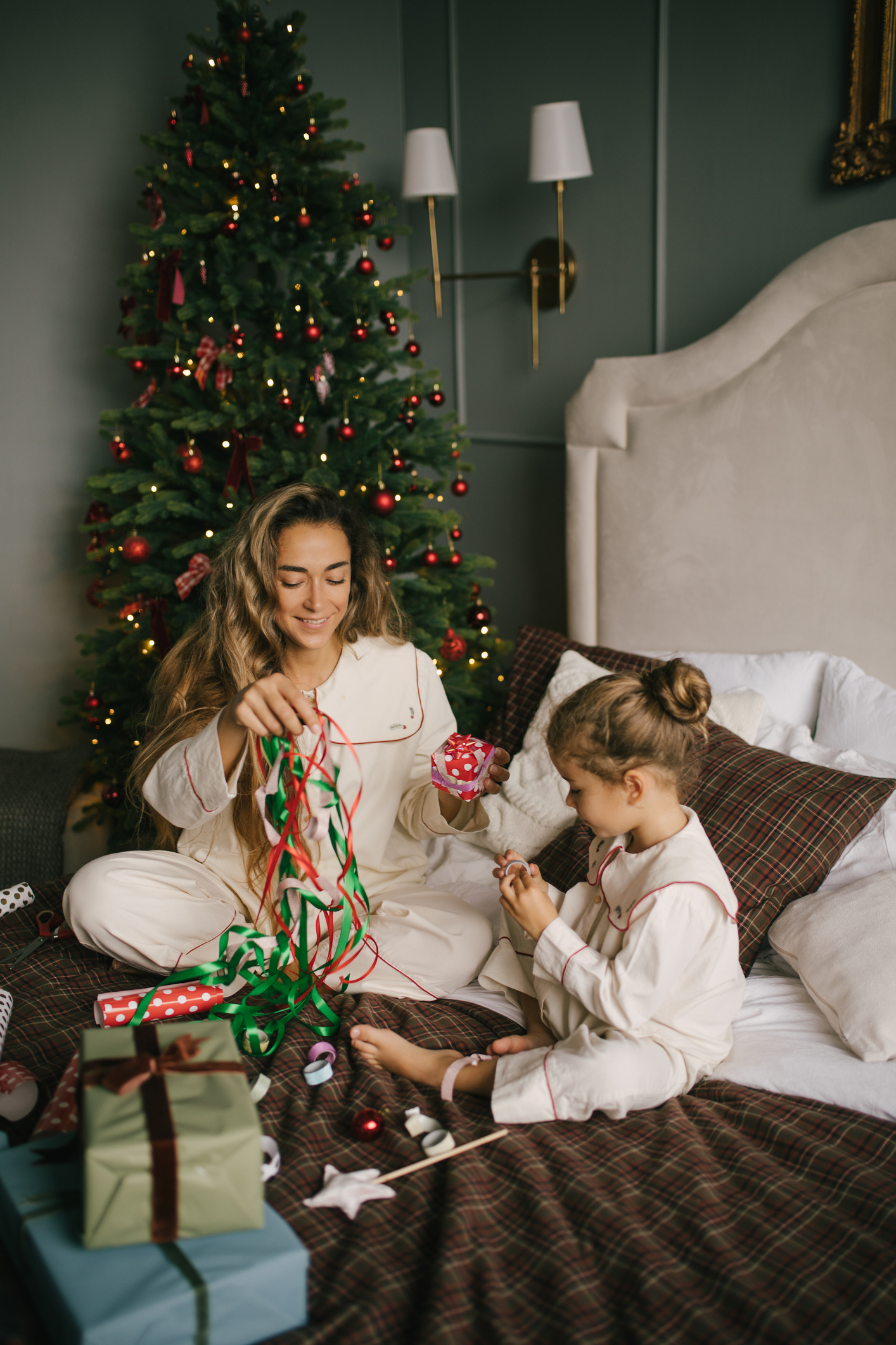mother and daughter packing and wrapping presents in a cosy, decorated bedroom with a Christmas tree.
