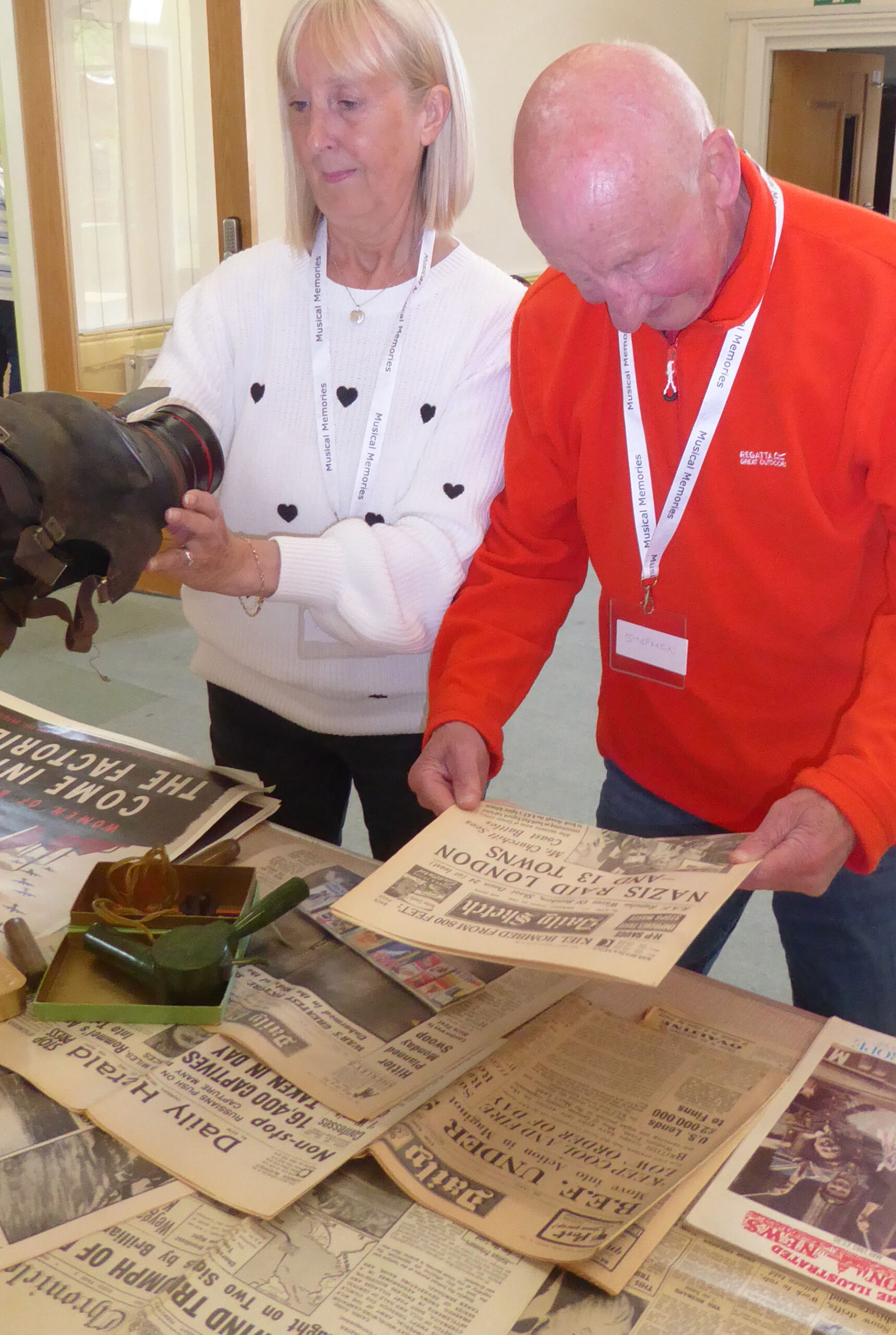 A couple examine the table of memories including a newspaper and gas mask
