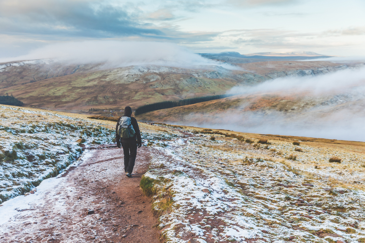 Man walking on snowy hills in Wales. Adult man hiking in winter, hills covered in snow and mist on background. Wanderlust, nature and exploration concepts.