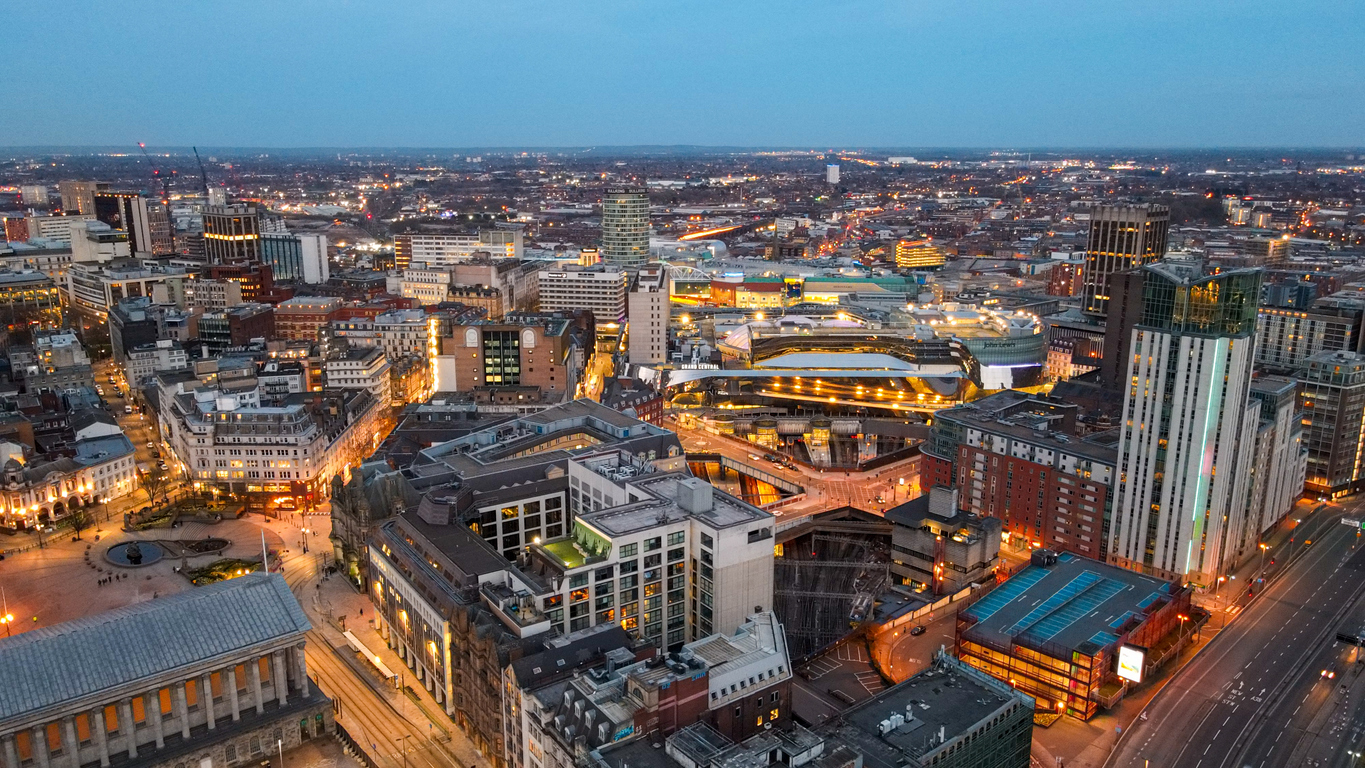 Captured with the DJI Mini 3 Pro, this stunning aerial image showcases Birmingham City Centre bathed in the soft, atmospheric glow of blue hour. The fading twilight casts a deep indigo hue over the skyline, while the city below begins to sparkle with life. Skyscrapers and historic buildings alike are illuminated, their windows glowing warmly against the cool tones of the evening sky. The iconic BT Tower and the modern silhouettes of the Library of Birmingham and The Cube stand out prominently, reflecting the vibrant pulse of the city. Streetlights trace the roads like glowing veins, and the last light of day gently kisses the horizon, creating a striking contrast between natural dusk and the artificial brilliance of the urban landscape.