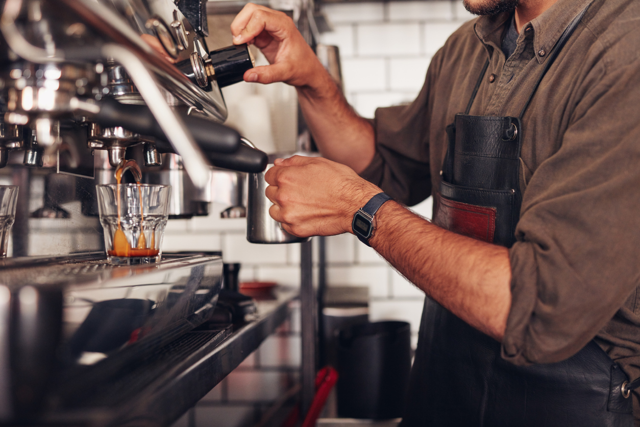 ropped shot of barista using a coffee maker to prepare a cup of coffee. Cafe worker making a coffee.