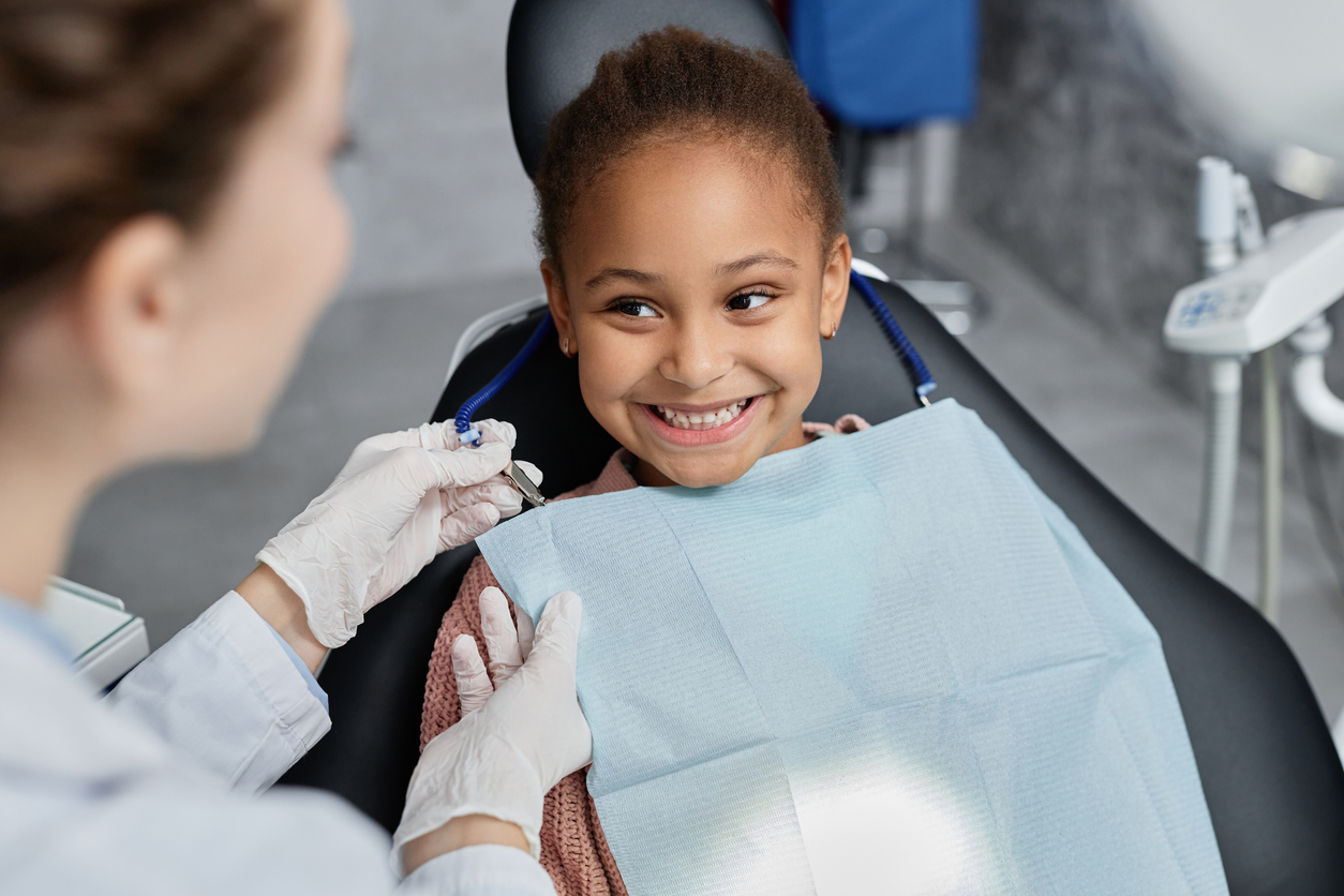 Portrait of smiling little girl in dental chair with nurse preparing her for teeth check up
