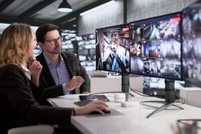 Security Guards Monitoring CCTV Footage In Control Room With Multiple Cameras.