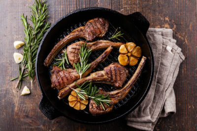 Roasted lamb ribs with rosemary and garlic on grill pan on dark wooden background