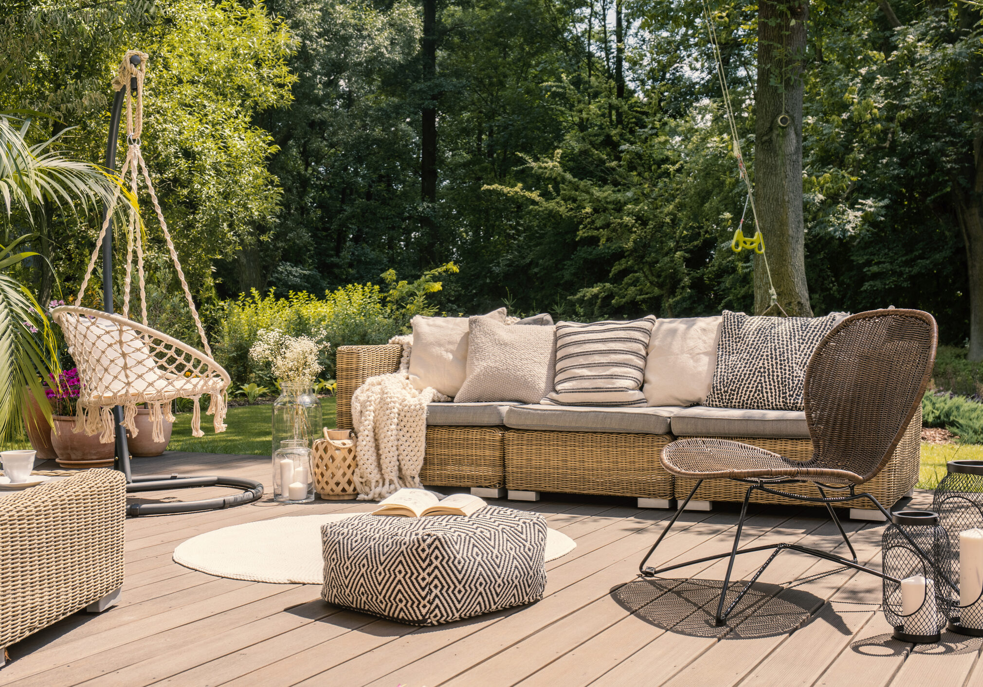 Pouf and rattan chair on wooden patio with settee in the garden during summer. Real photo