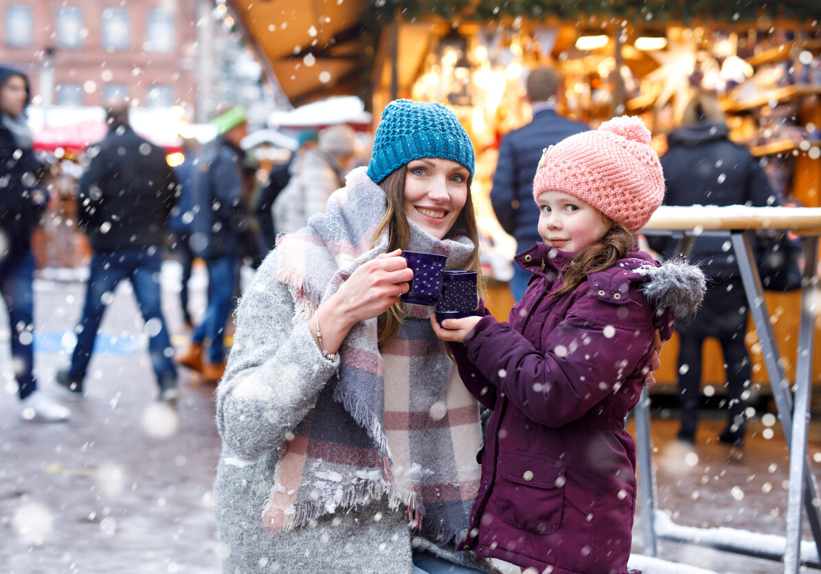 Happy kid girl and young beautiful woman with cup of steaming hot chocolate and mulled wine. Adorable child and beautiful mum on Christmas market in Germany. Family walking on Xmas market