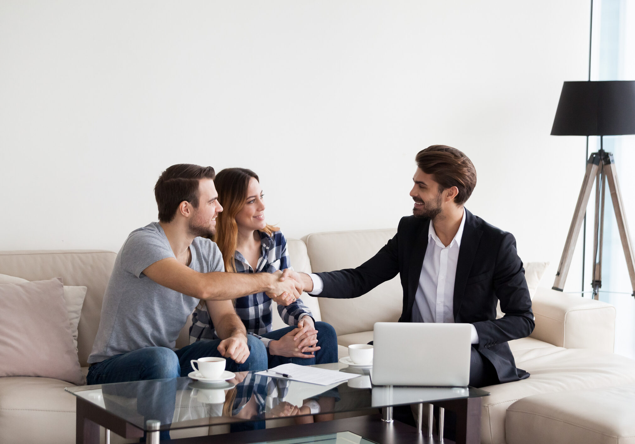 Young couple, family at meeting with Real Estate Agent, interior designer, decorator, landlord making deal. Husband handshaking with man in suit. Concept of meeting with client, customer