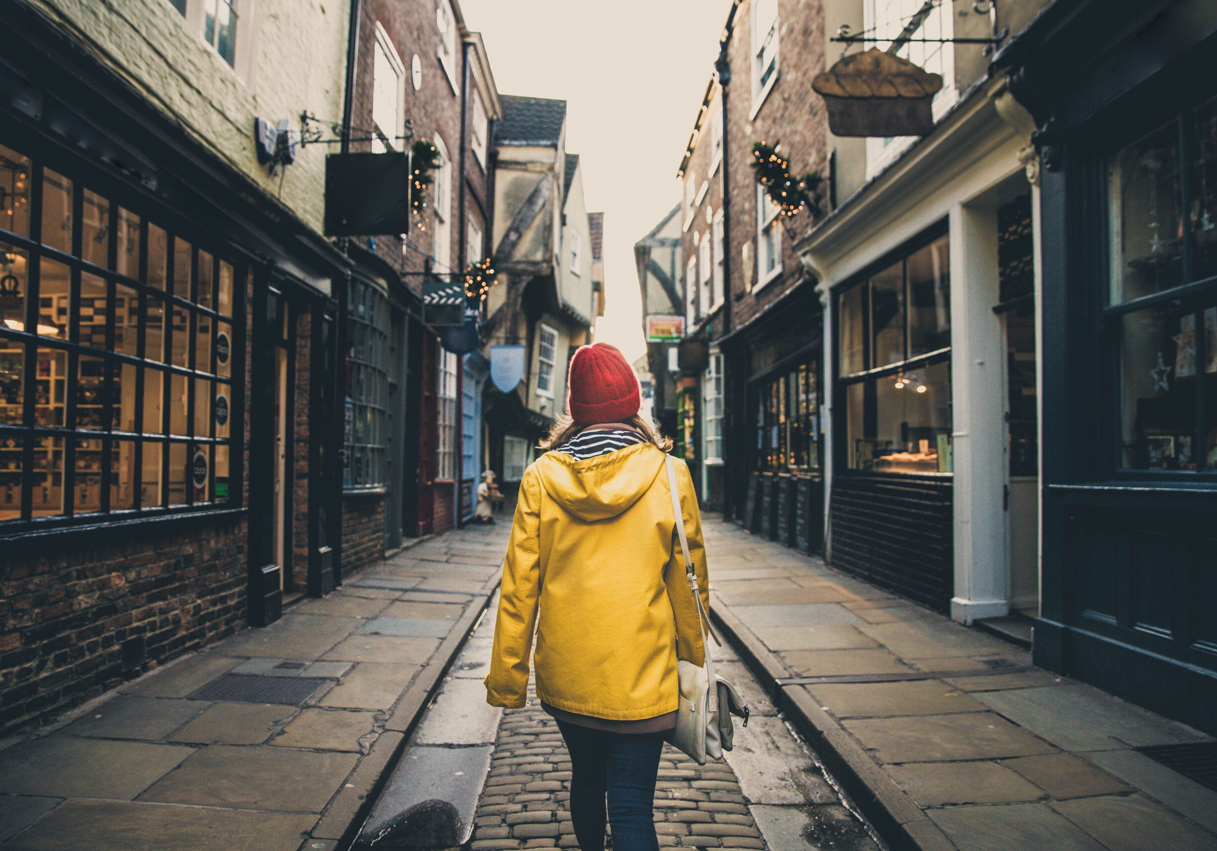 A rear view of a female in a bright yellow coat walking along the historic street known as The Shambles in York, UK which is a popular tourist destination in this Yorkshire city.