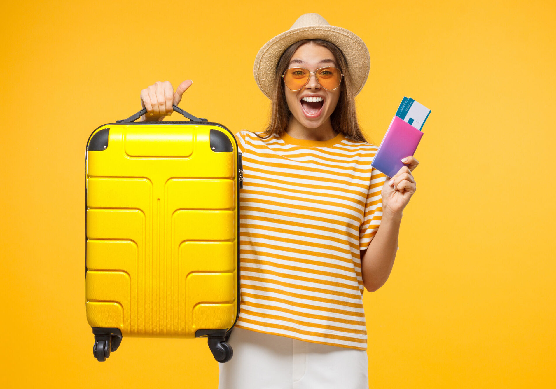 Happy European girl with suitcase and airplane tickets isolated on yellow background excited about trip