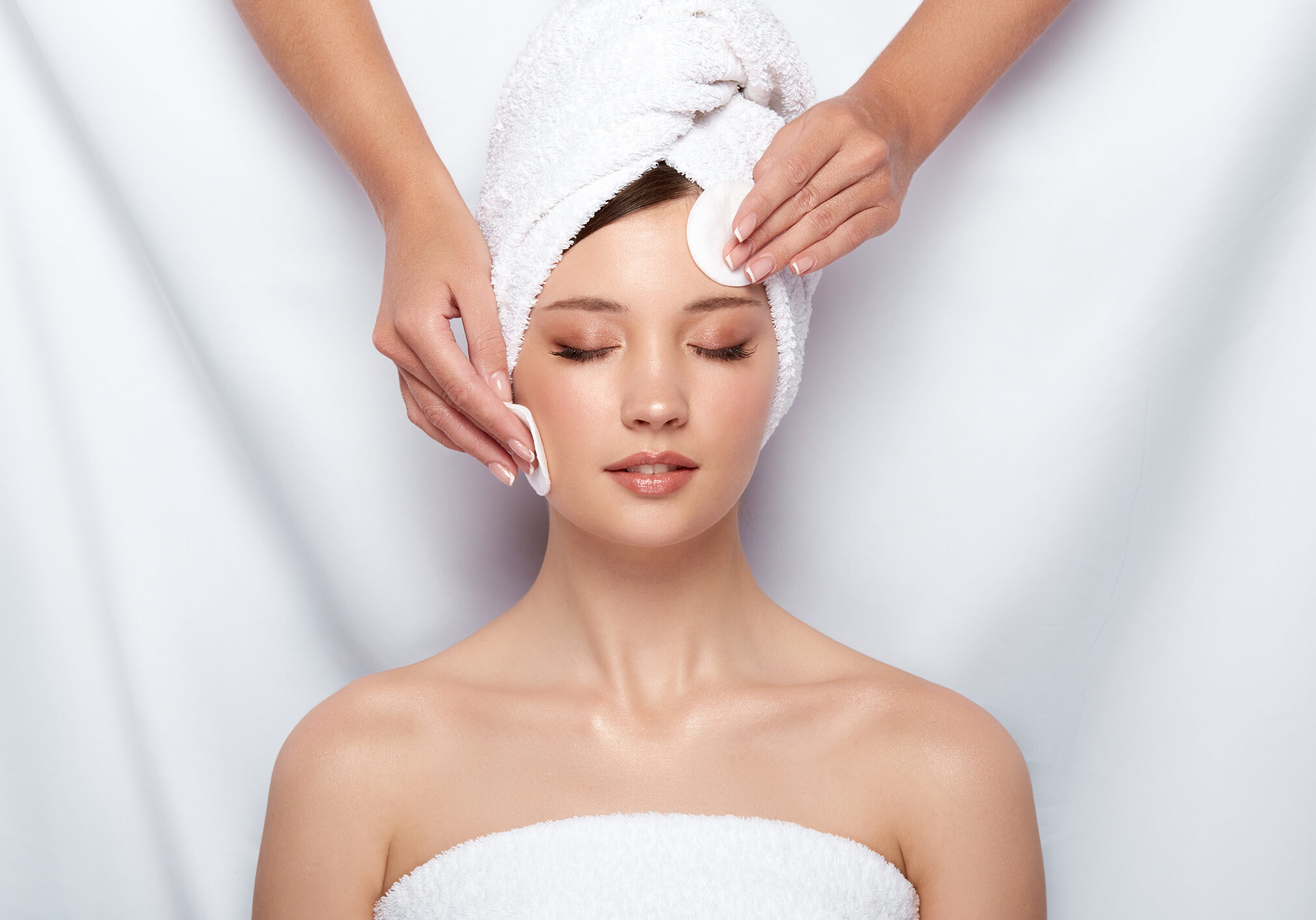 beautician wiping woman's face with cotton pads, girl gets facial treatment, female arms cleans body with two sponges in spa