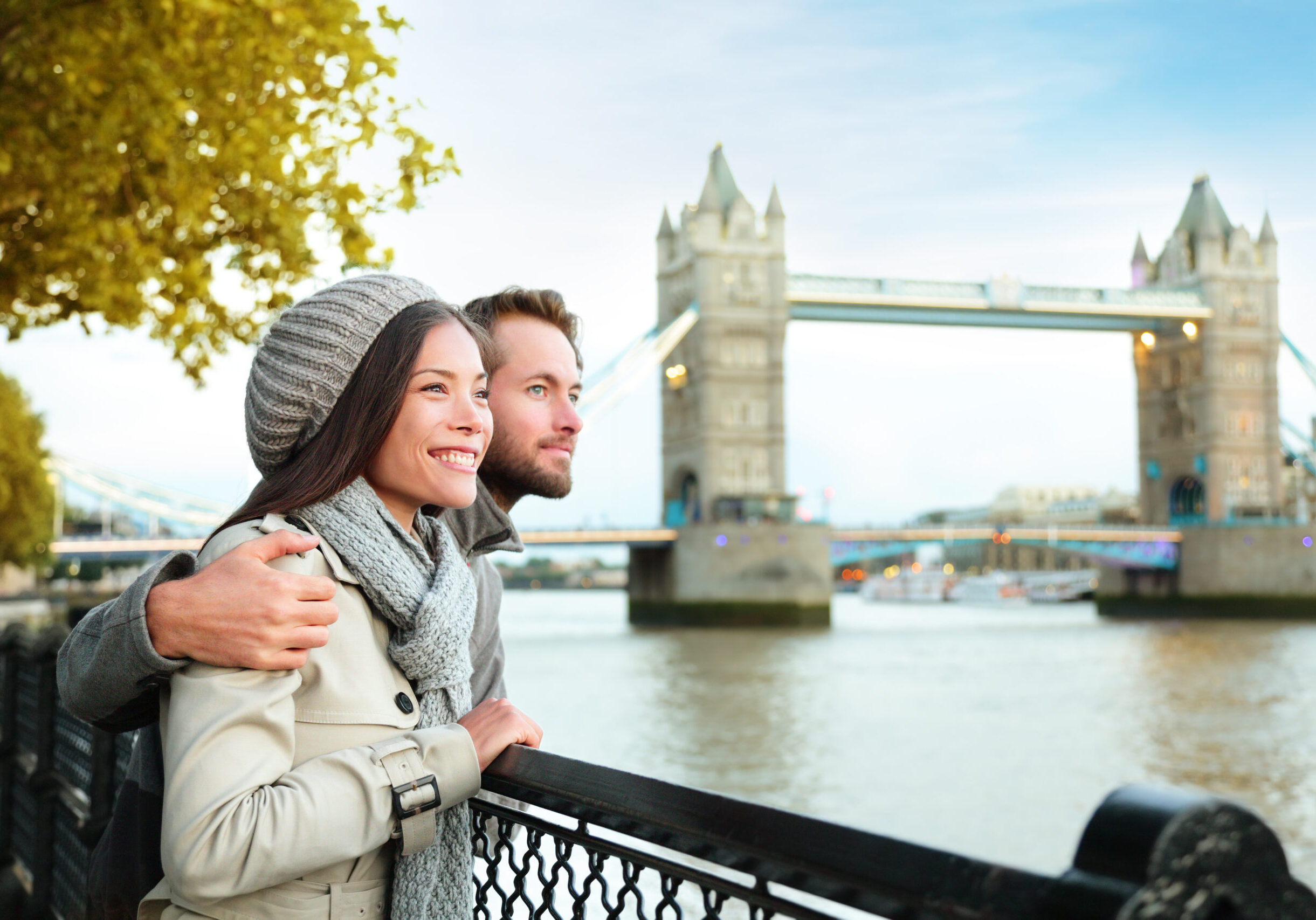 Happy couple by Tower Bridge, River Thames, London. Romantic young couple enjoying view during travel. Asian woman, Caucasian man in London, England, United Kingdom.