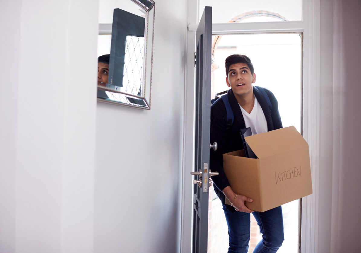 Male College Student Carrying Box Moving Into Accommodation