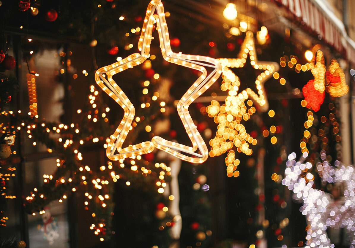 Stylish christmas golden star illumination and fir branches with red and gold baubles, golden lights bokeh on front of building at holiday market in city street. Christmas street decor