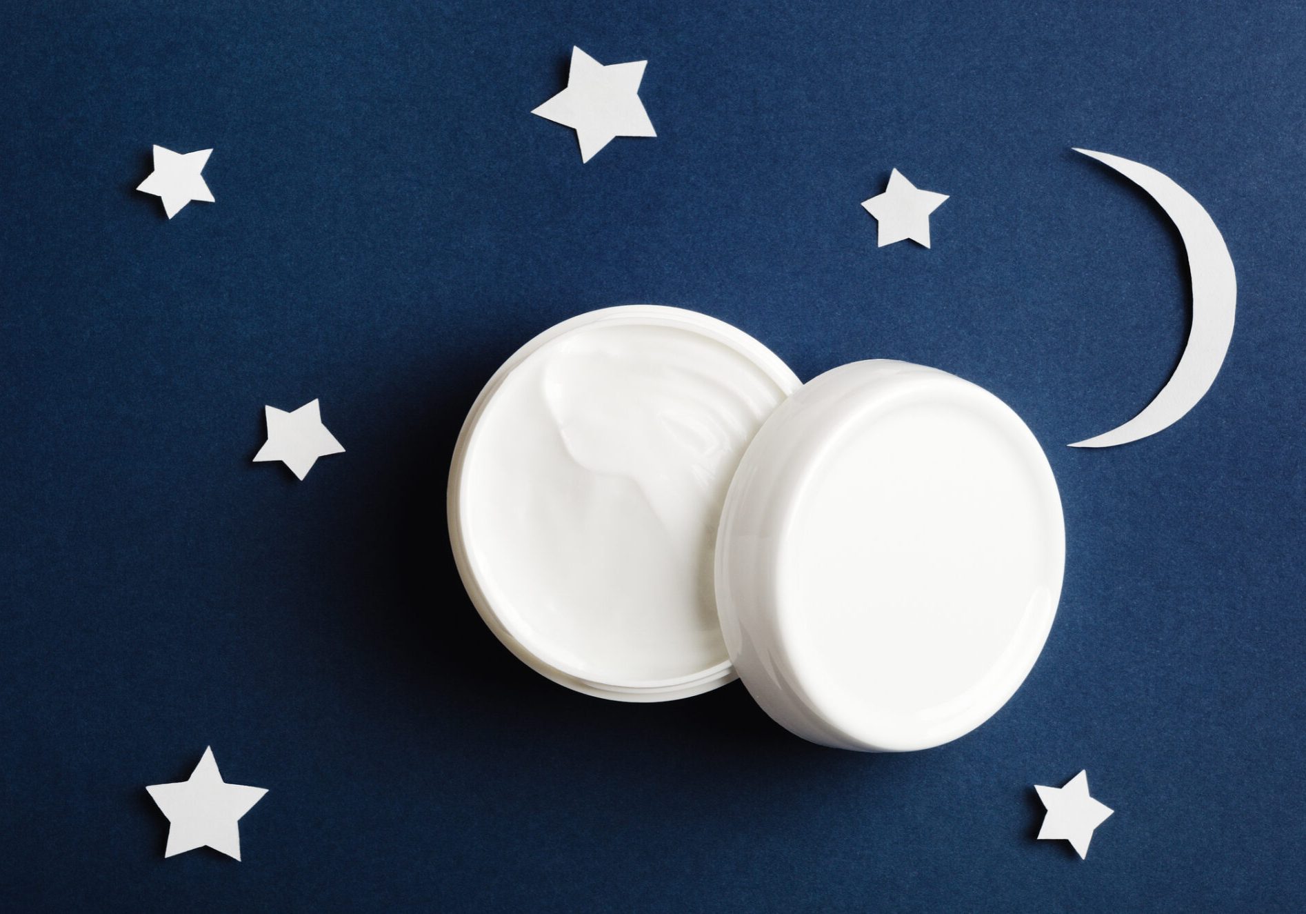 Cosmetic white container on night sky background top view. Skincare cosmetology product, night care concept. Organic cosmetics. Hand, face, body moisturizing cream jar. Women present idea.