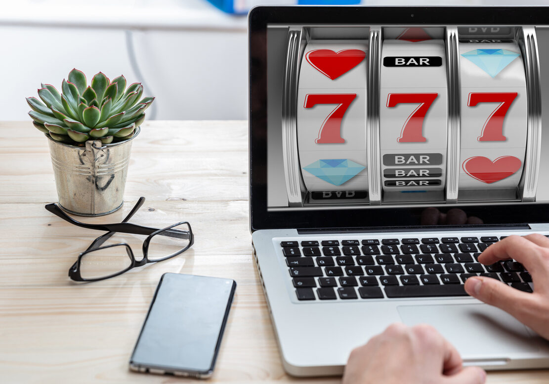 Slot machine, online casino gambling concept. Man working with a computer laptop, 777 on the screen, office business background.