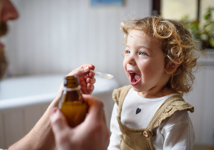 Unrecognizable mature father givingsyrup to small sick daughter indoors at home.