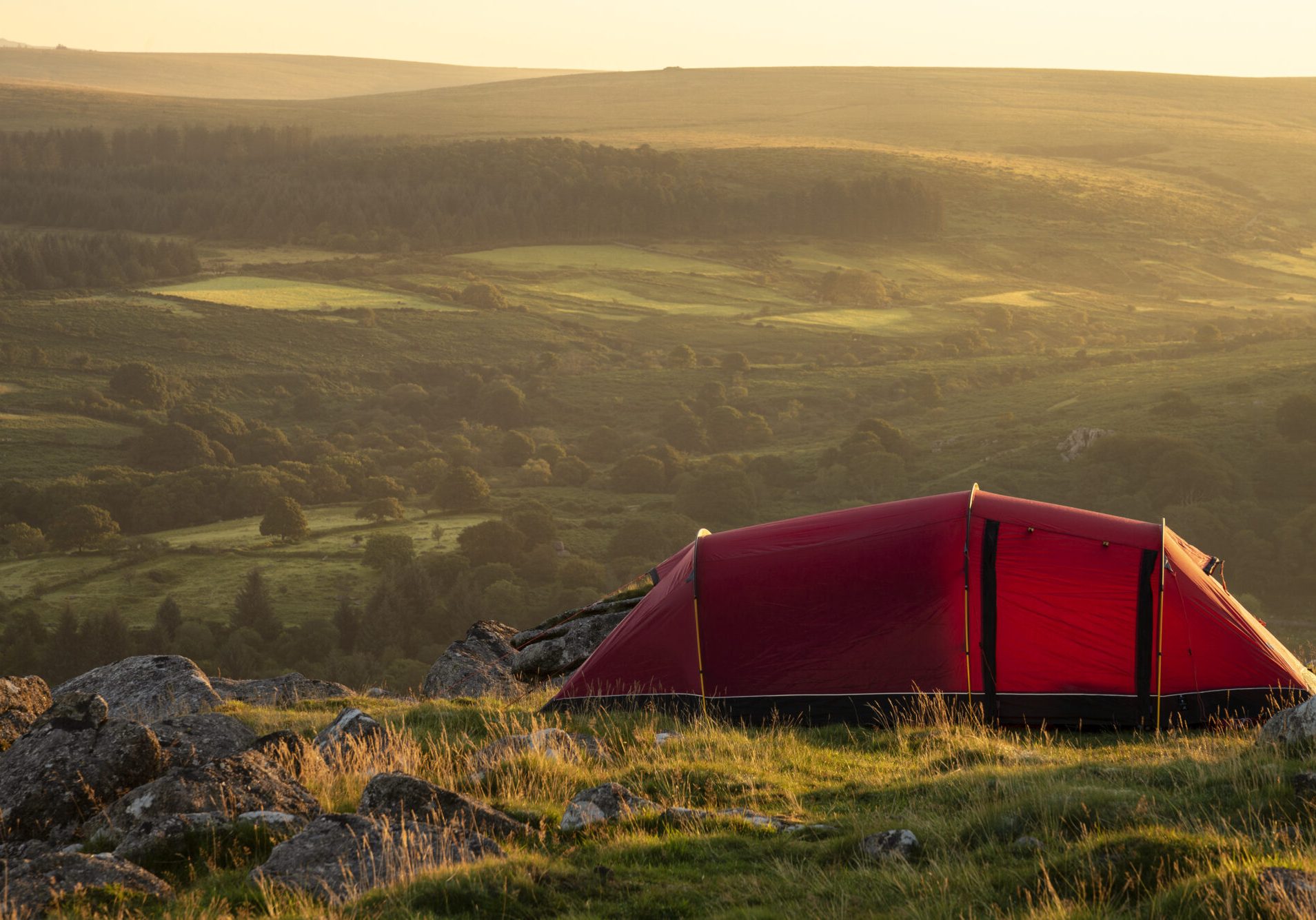 Beautiful image of wild camping in English countryside during stunning Summer sunrise with warm glow of the sun lighting the landscape