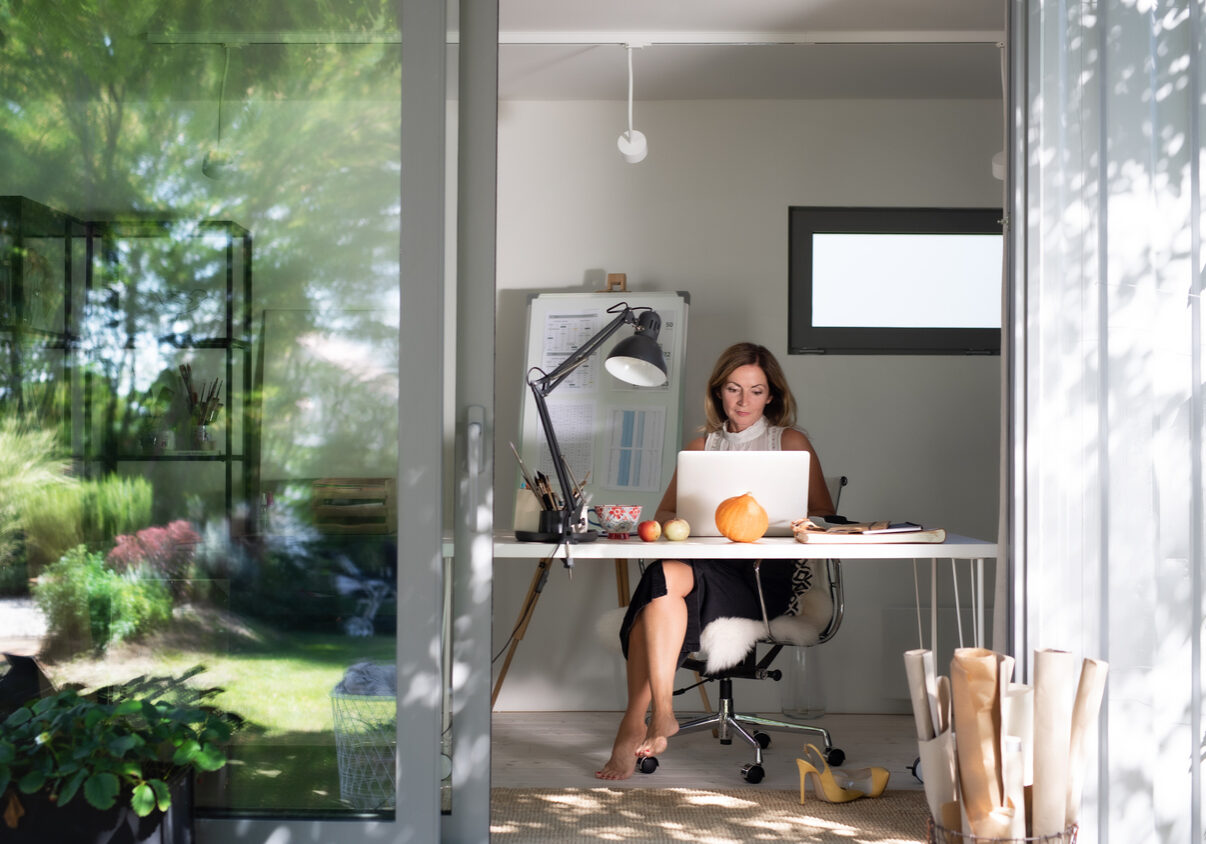 Front view of mature woman working indoors in home office in container house in backyard.