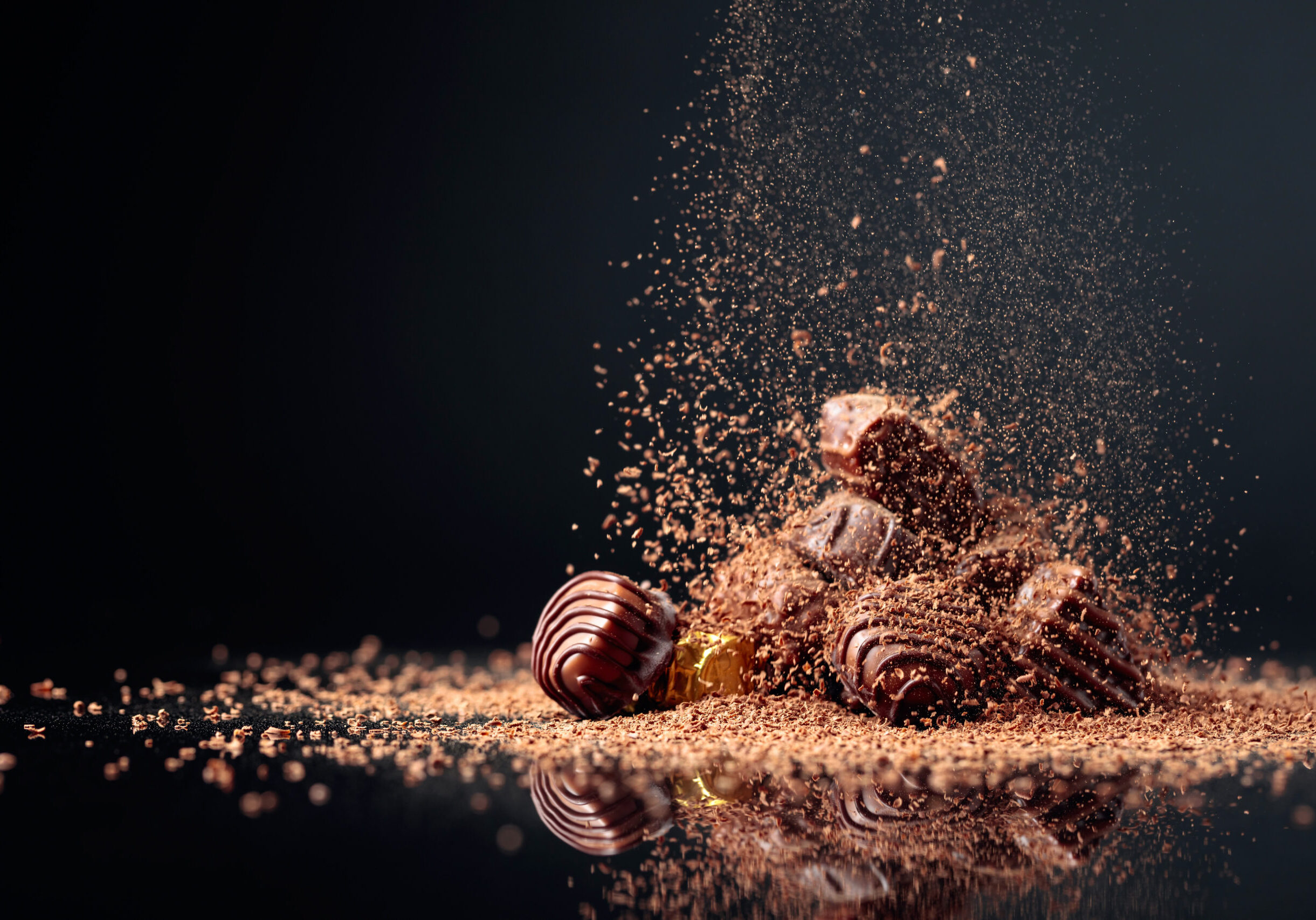 Various chocolate candies on a black background sprinkled with chocolate chips. Copy space.