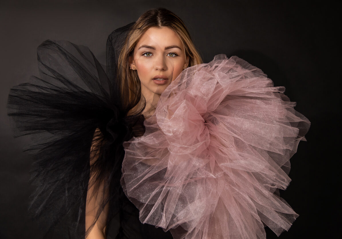 Studio photo of beautiful young woman wearing makeup and mesh evening dress while posing against black background, copy space, beauty concept for advertising parfume, looking through textile