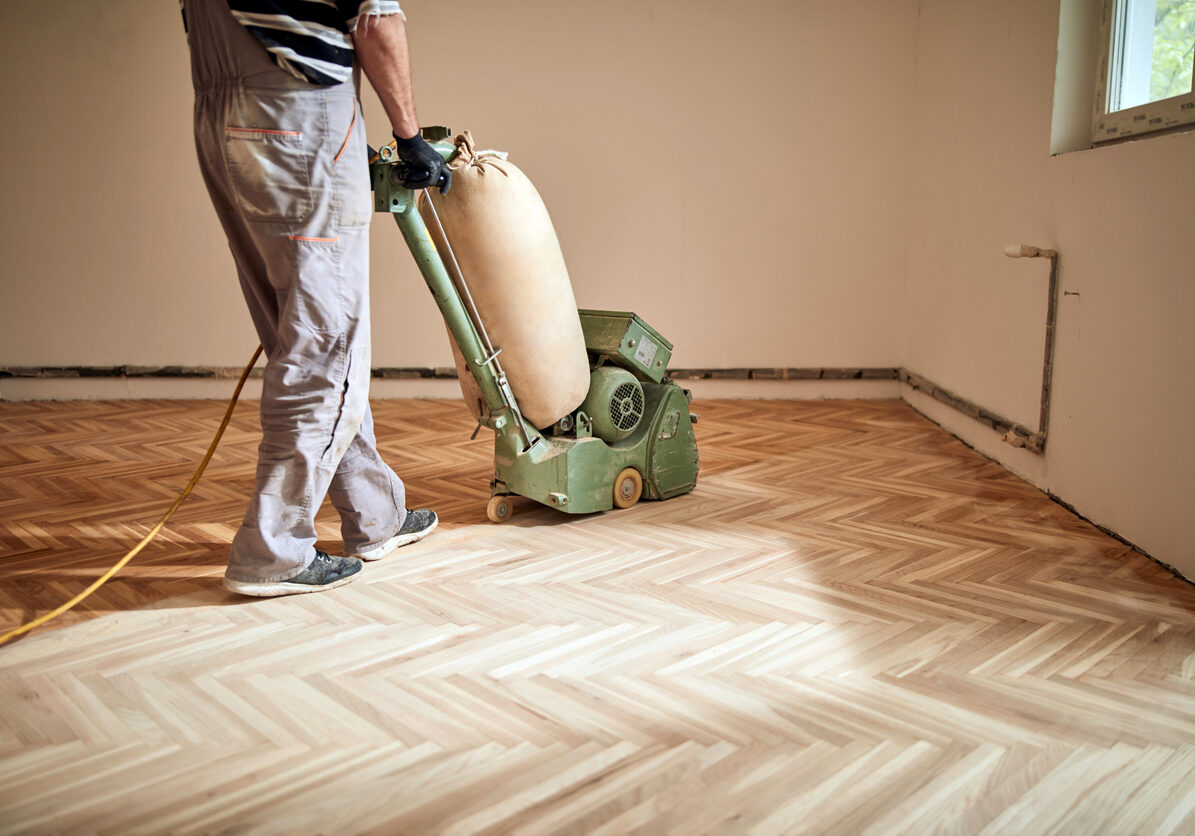 Repairman restoring parquet with a sanding machine.