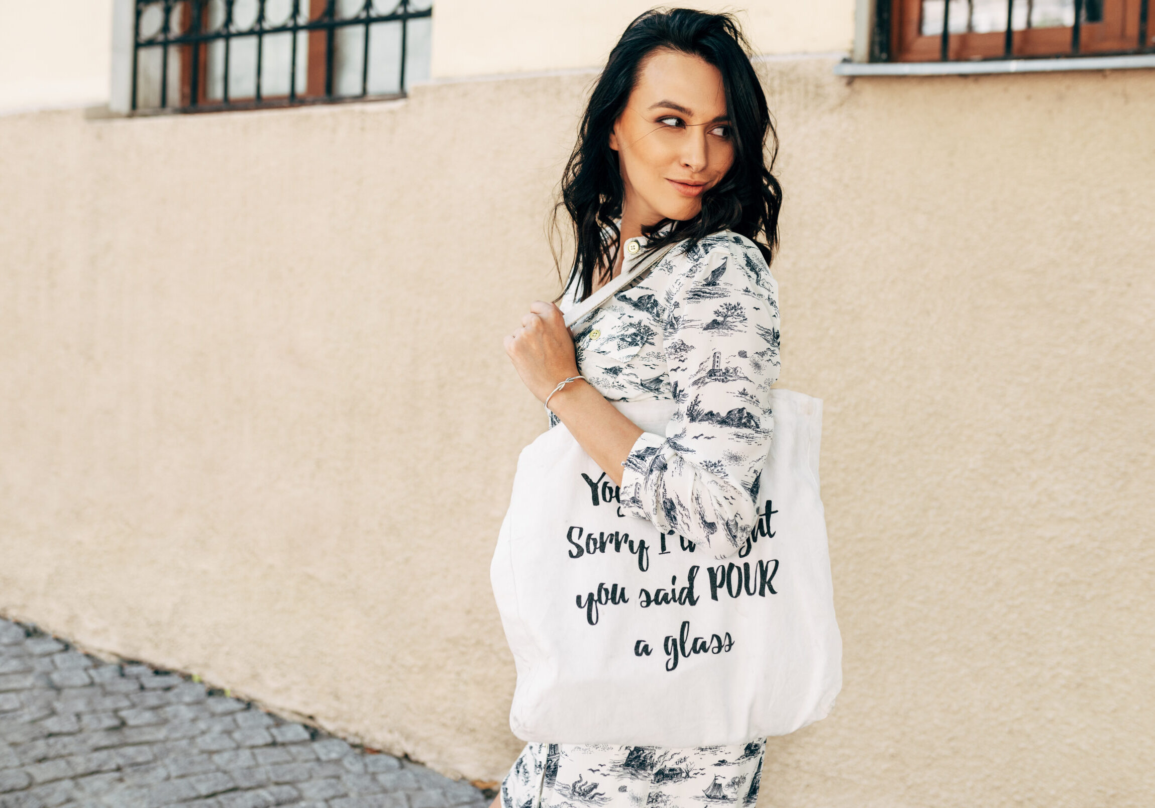 Horizontal outdoor shot of a beautiful young woman walking to the grocery with an eco bag in the street. Pretty girl posing with a reusable textile bag on a sunny day.