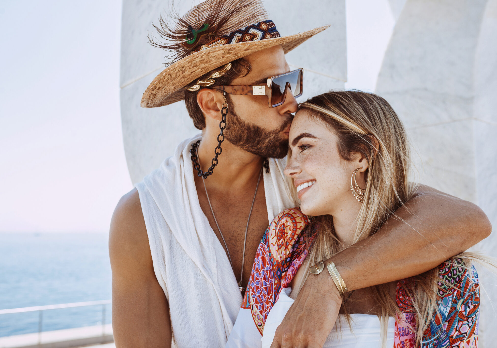 Close up of attractive young couple embracing on beach. Bearded man kissing blonde woman on forehead. Sea background on beautiful morning light at summer