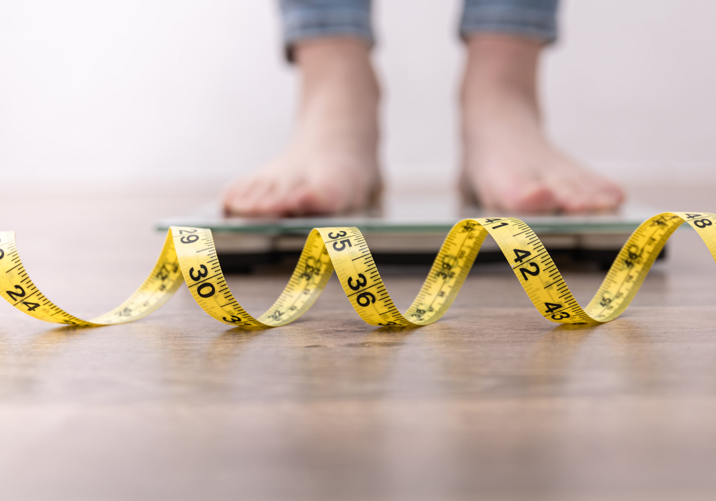 Women's legs on the scales, close-up of a measuring tape, the concept of losing weight, healthy lifestyle.