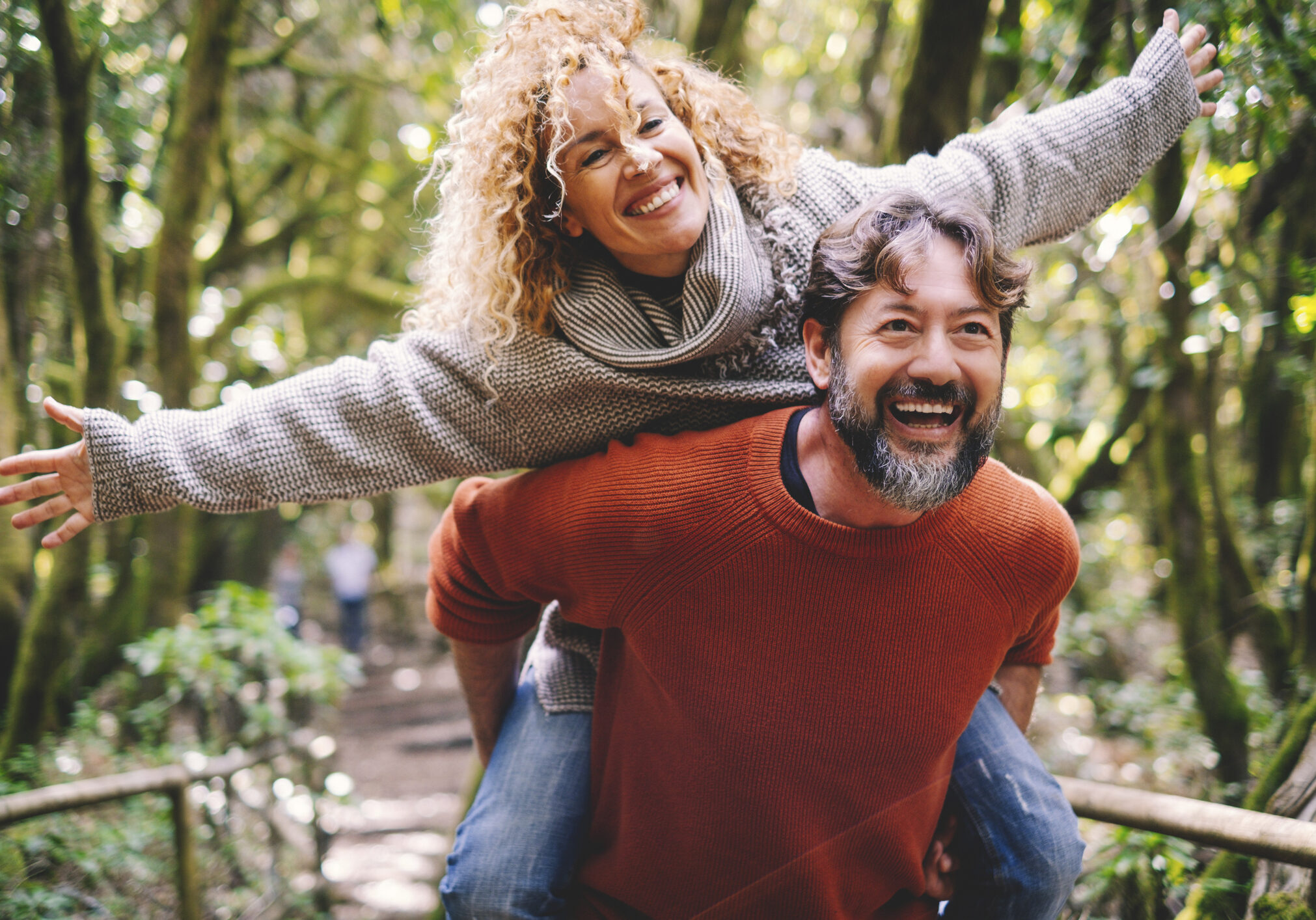 Overjoyed adult couple have fun together at outdoor park in leisure activity. Man carrying woman in piggyback and laugh a lot. Love and life mature people lifestyle concept. Enjoying vacation nature