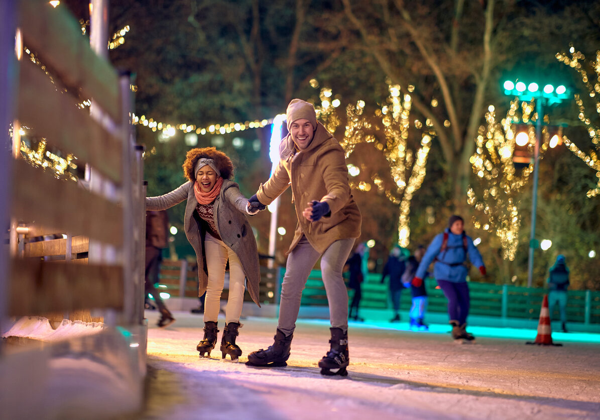 Jolly multiethnic couple enjoying night ice skating together