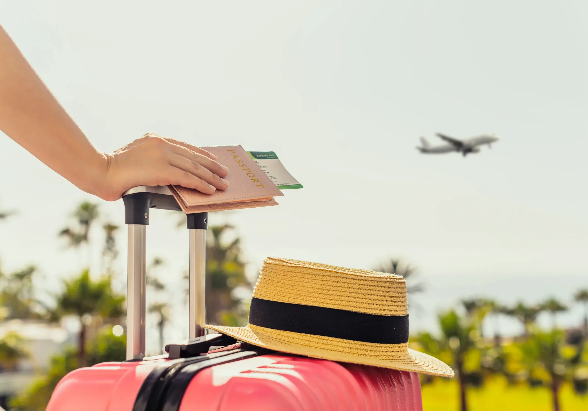 Woman with pink suitcase and passport with boarding pass standing on passengers ladder of airplane opposite sea with palm trees. Tourism concept