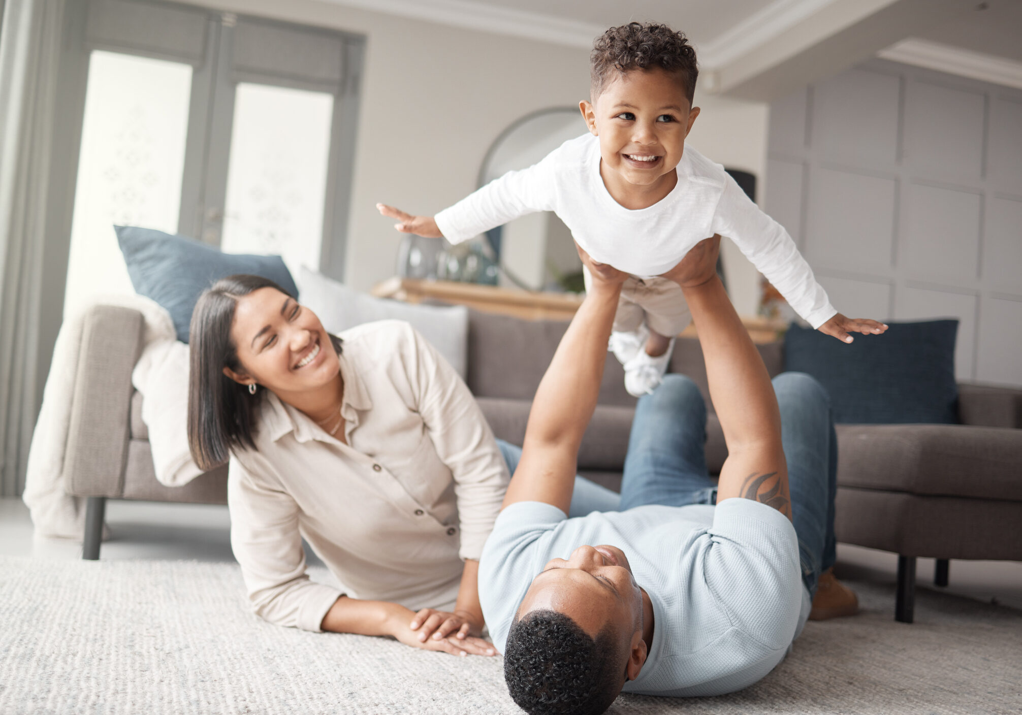 A happy mixed race family of three relaxing on the lounge floor and being playful together. Loving black family bonding with their son while playing fun games on the carpet at home