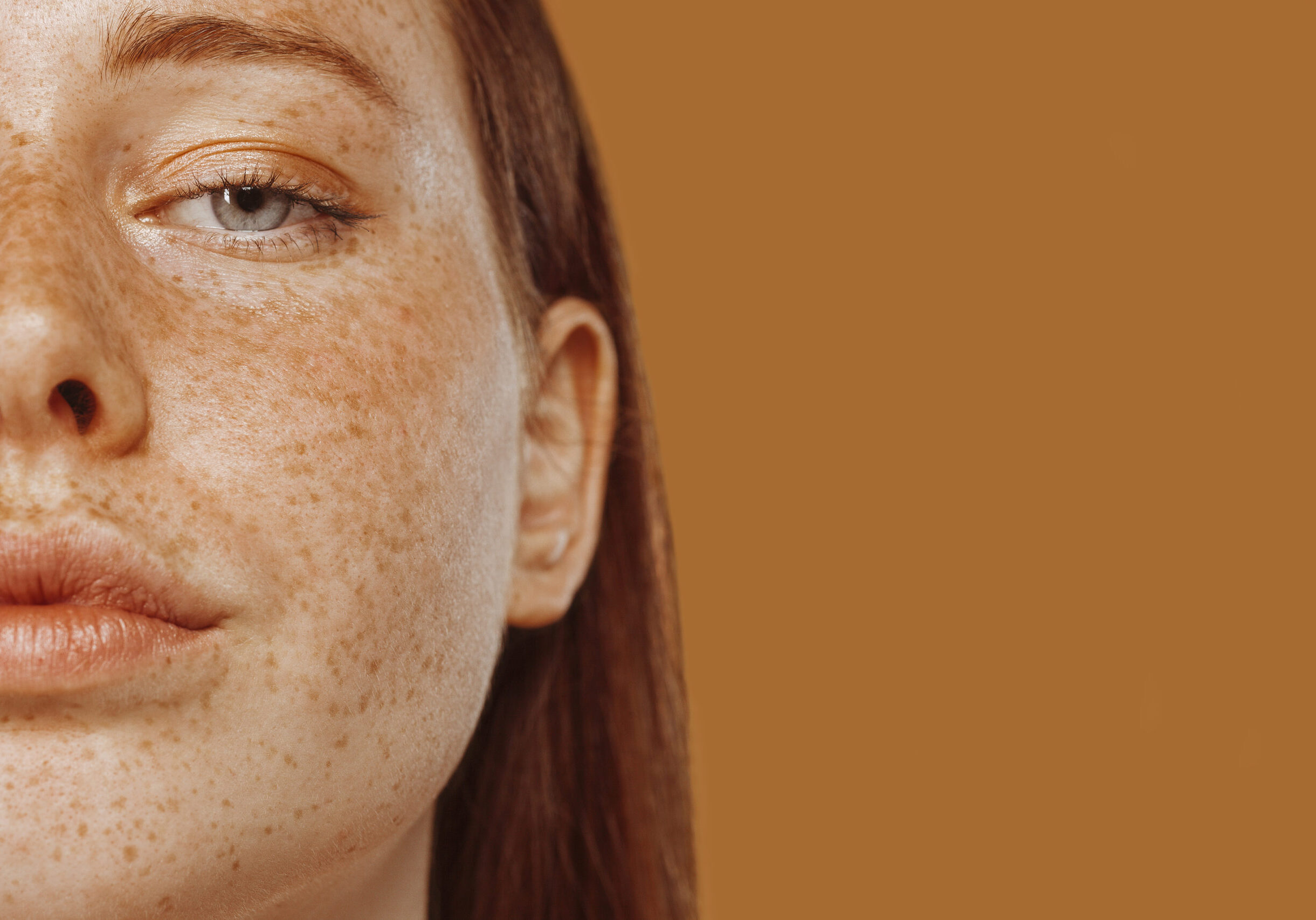 Close-up portrait of half face red-haired girl with freckle and blue eye. Beautiful young woman's face shot. Female model with perfect skincare, human emotions, facial expression, beauty and cosmetics concept.