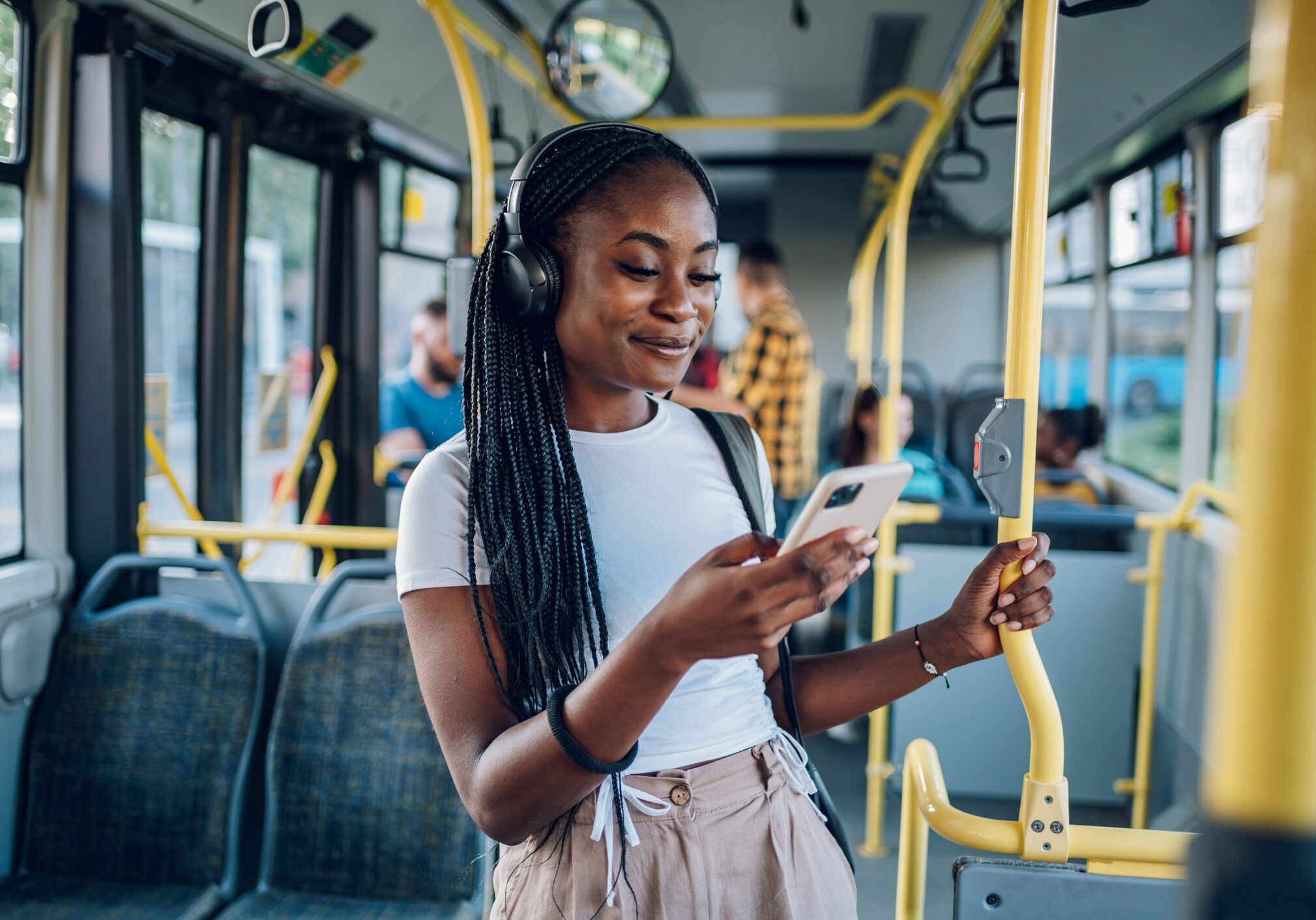 Young African american woman wearing earphones and listening to music on a smartphone while standing alone on a bus. Traveling to work and enjoying a bus ride. Portrait of a beautiful black woman.