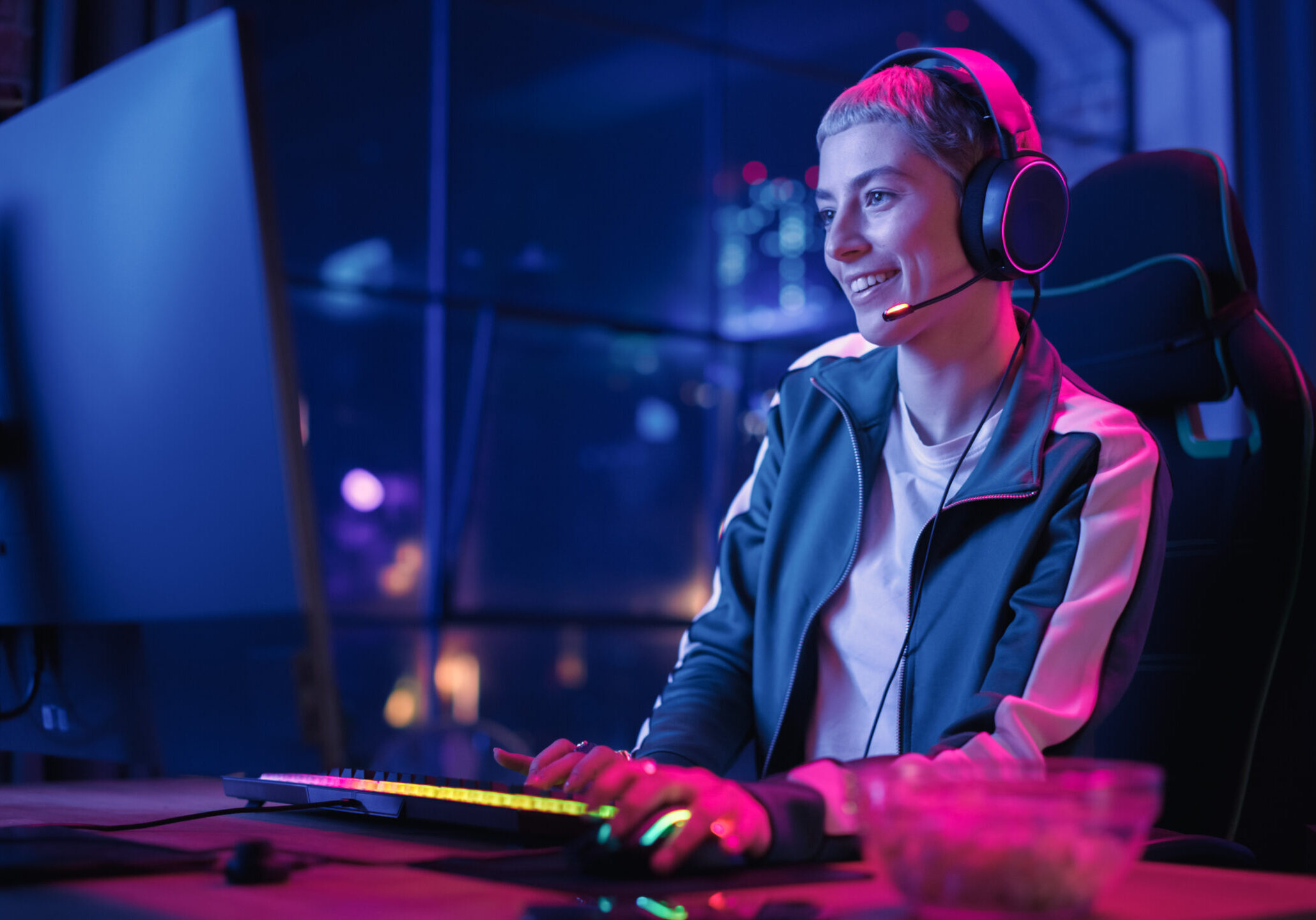 Excited Female Gamer Playing Online Video Game on Computer. Portrait of Young Woman in Headphones Battling in PvP Tournament with Other Players, Talking with Team on Microphone.