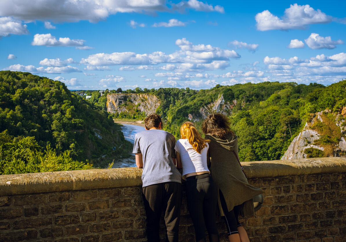 Mature mother with teenage son and daughter standing on tall bridge enjoying the view on sunny summer day; blue sky with clouds in background