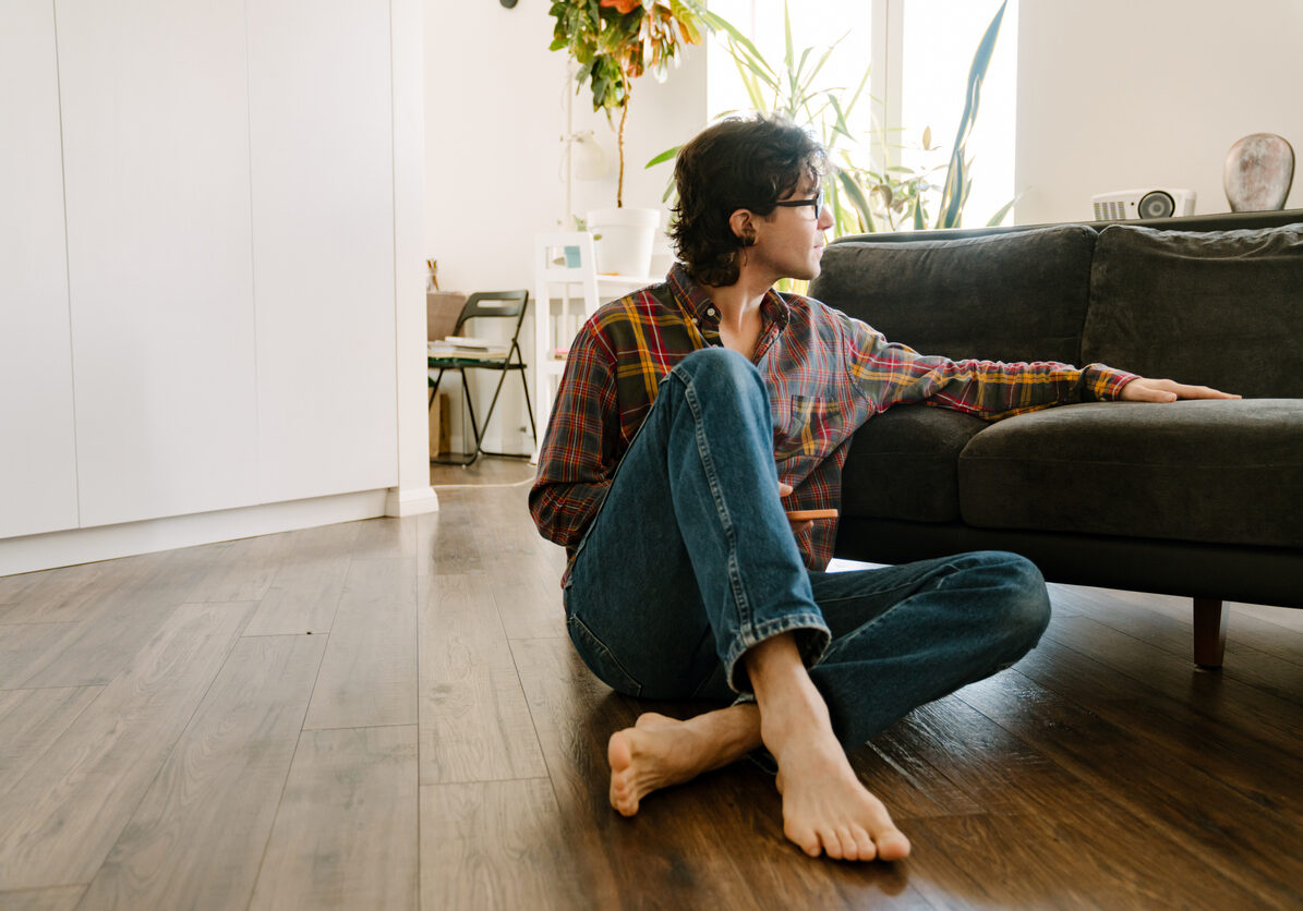 White man in glasses using mobile phone while sitting on floor at home