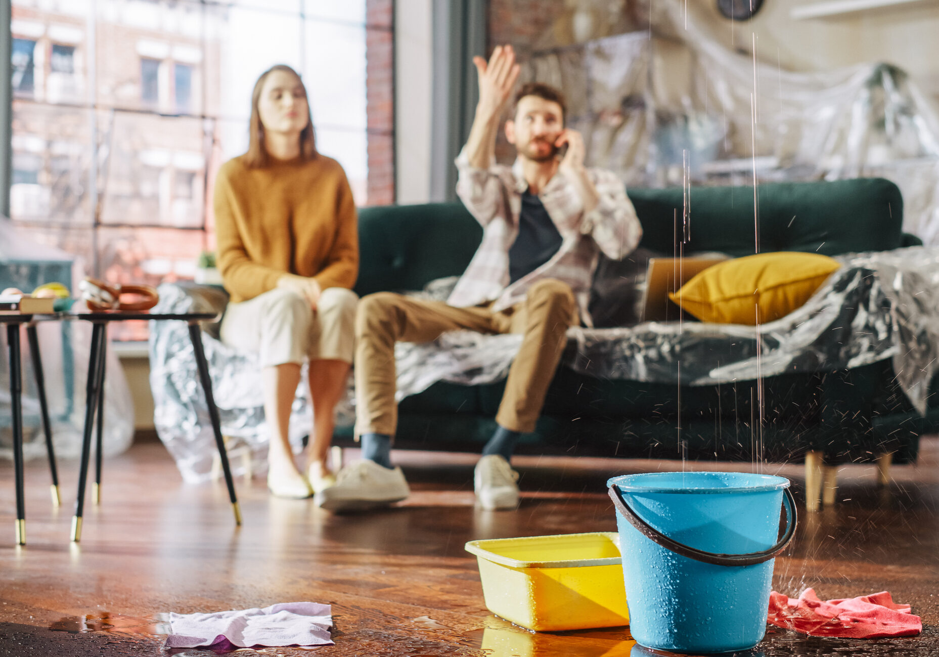 Roof is Leaking, Pipe Rupture at Home: Water Drips into Buckets in Living Room. Angry Couple in Background Calling Insurance Company, Screaming into Phone in Frustration, Trying to Find Plumber