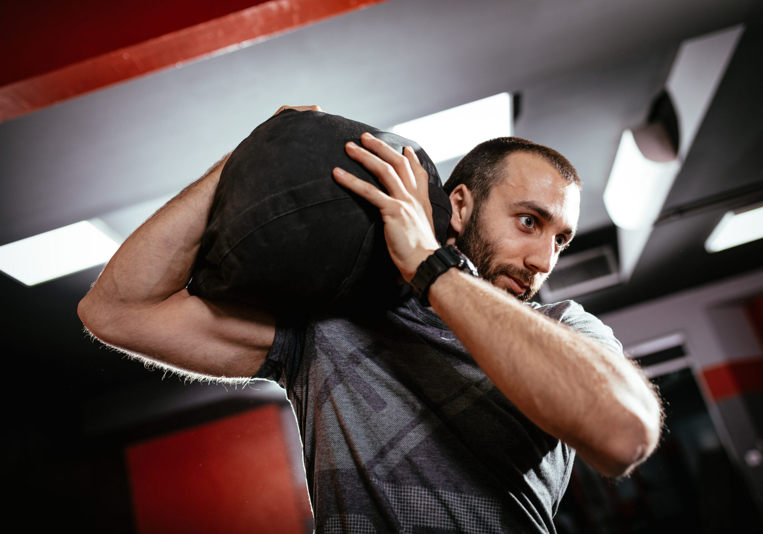 Strong man doing cross training with sandbag at the gym.