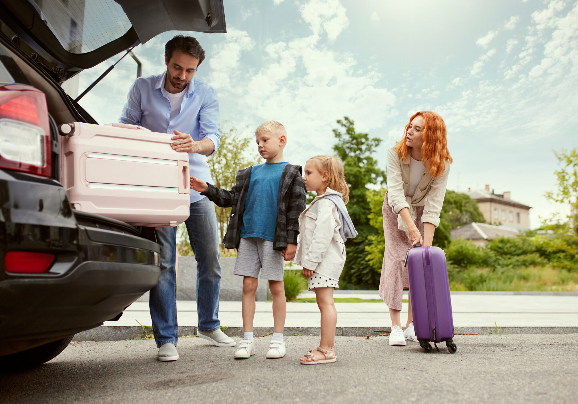 Man and woman, parents going on vacation with their children, packing suitcases into car. Car trip. Weekend adventures. Concept of family, childhood and parenthood, travelling, vacation, ad