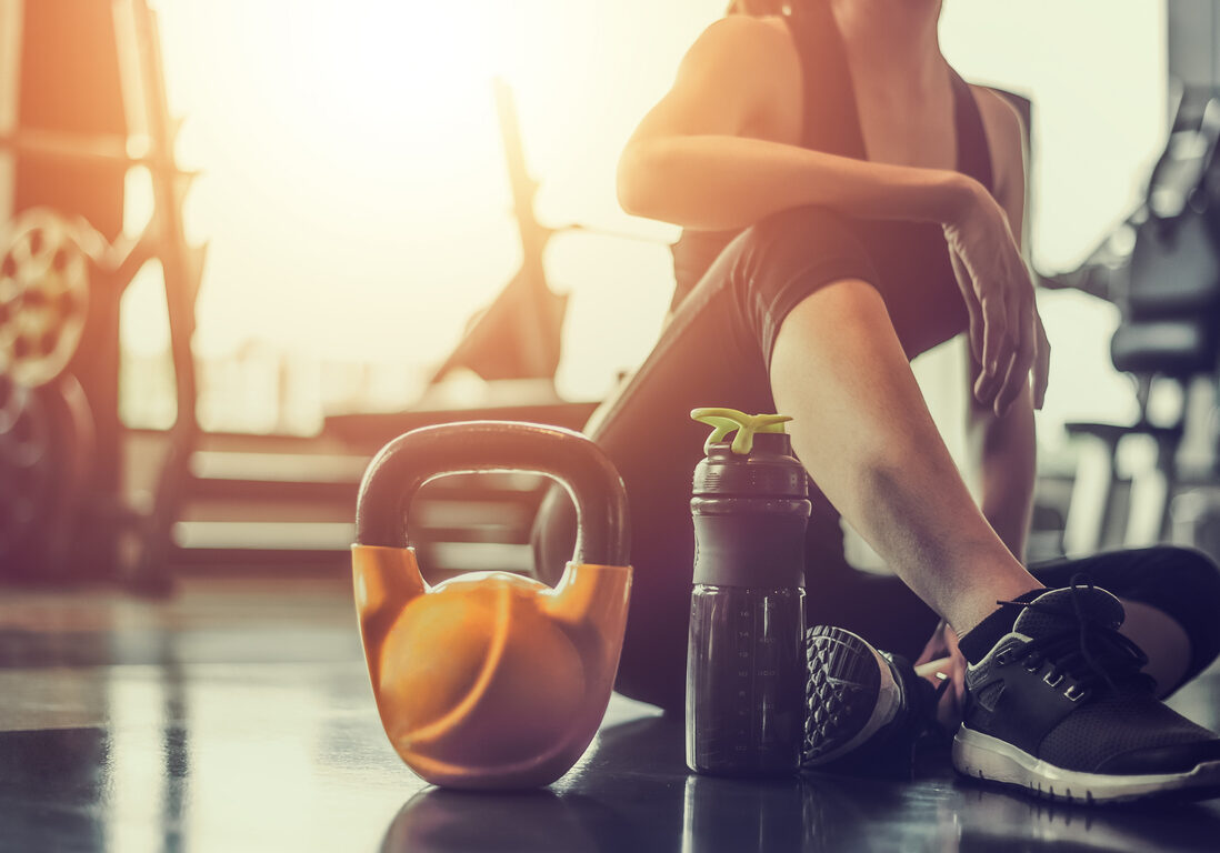 Concepts healthy lifestyle and workout. Bodybuilder, Workout, Fitness, Gym. Young asian woman sitting taking a break relaxing after exercise with a whey protein and dumbbell placed beside at gym.
