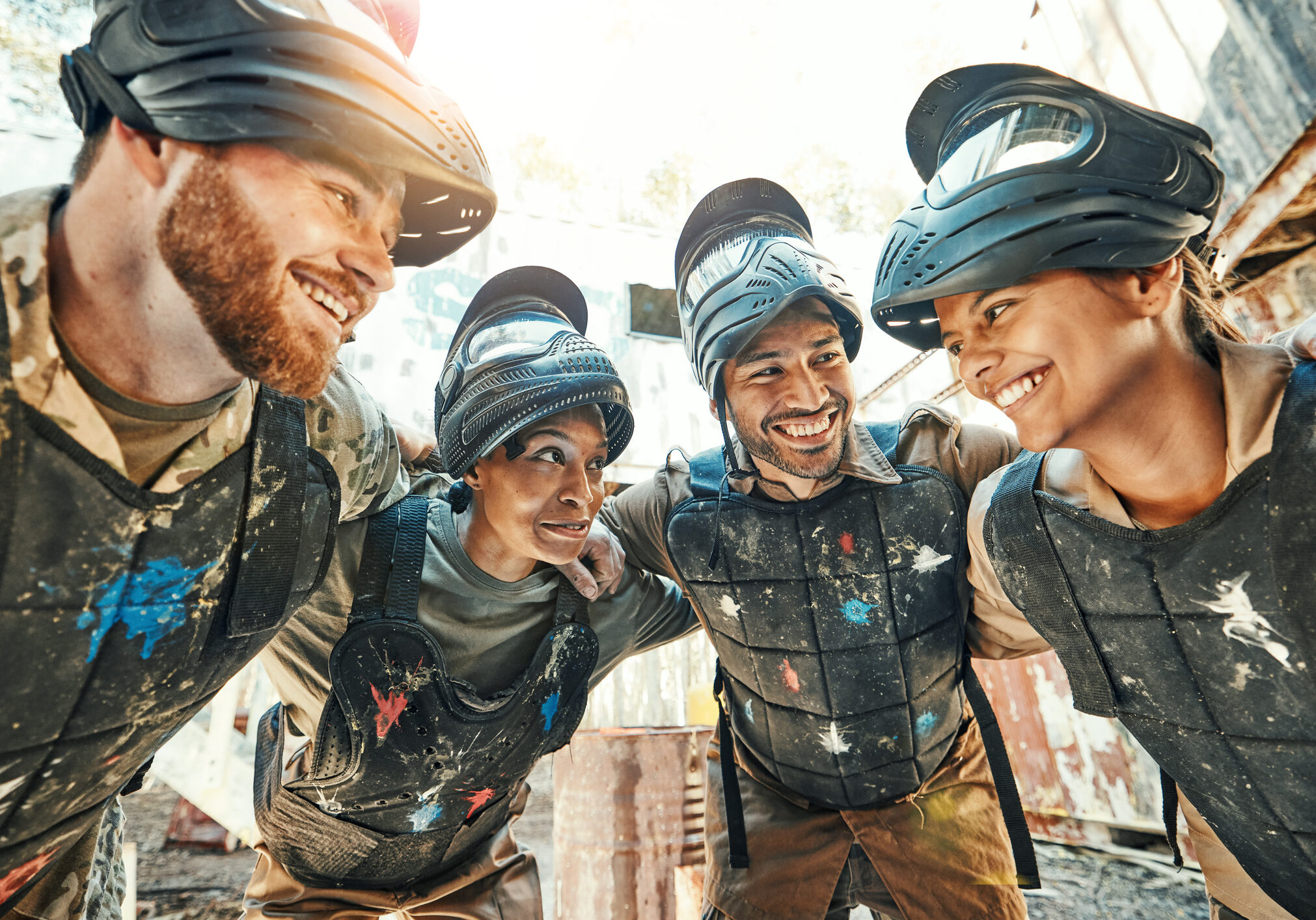 Paintball, happy team and meeting in huddle for game plan, collaboration or strategy on battle field together. Group of paintballers smile in war discussion, teamwork or motivation before match start