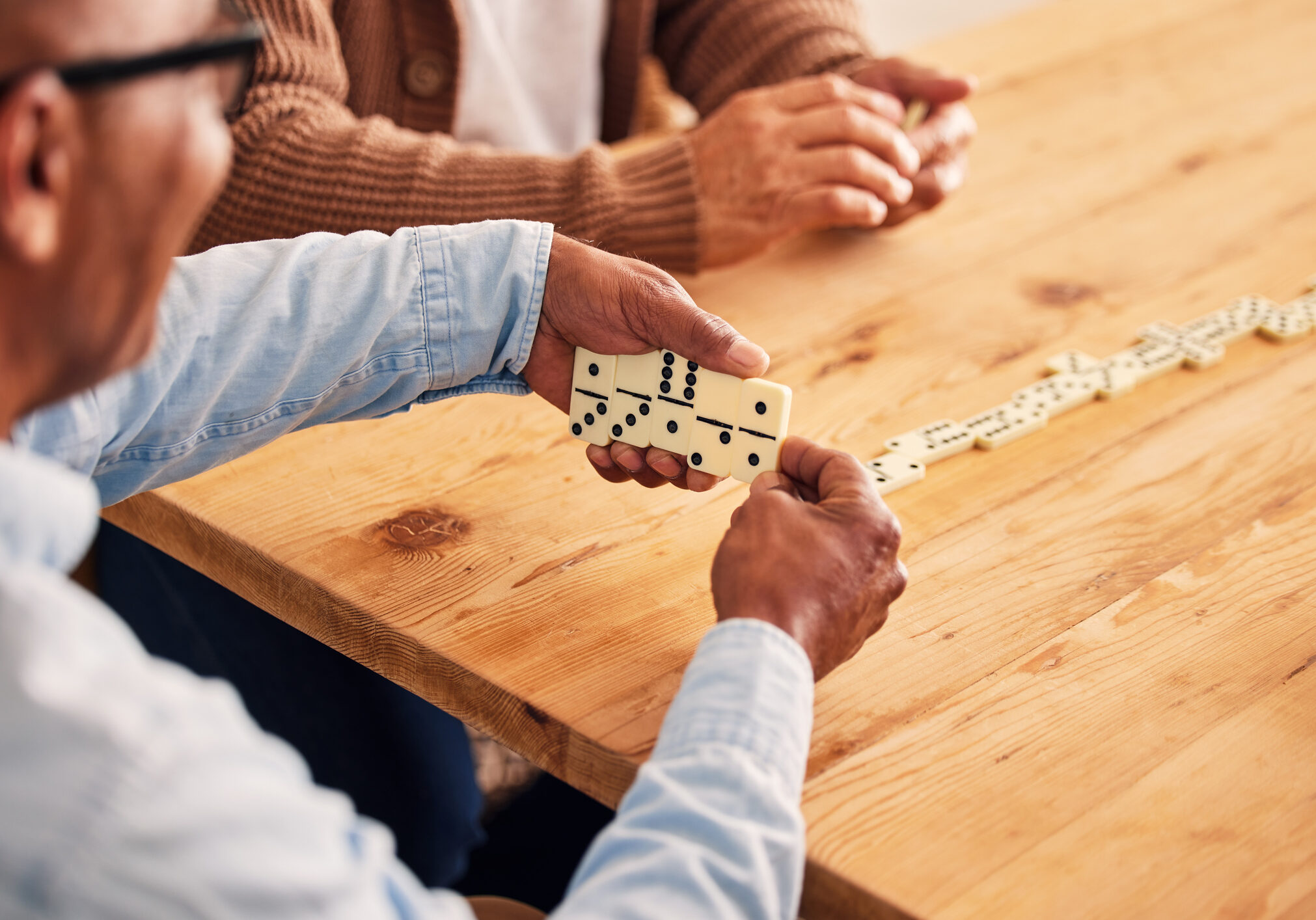 Hands, dominoes and a senior man playing a game at a table in the living room of a retirement home. Thinking, strategy and fun with an elderly male pensioner in a house closeup for entertainment