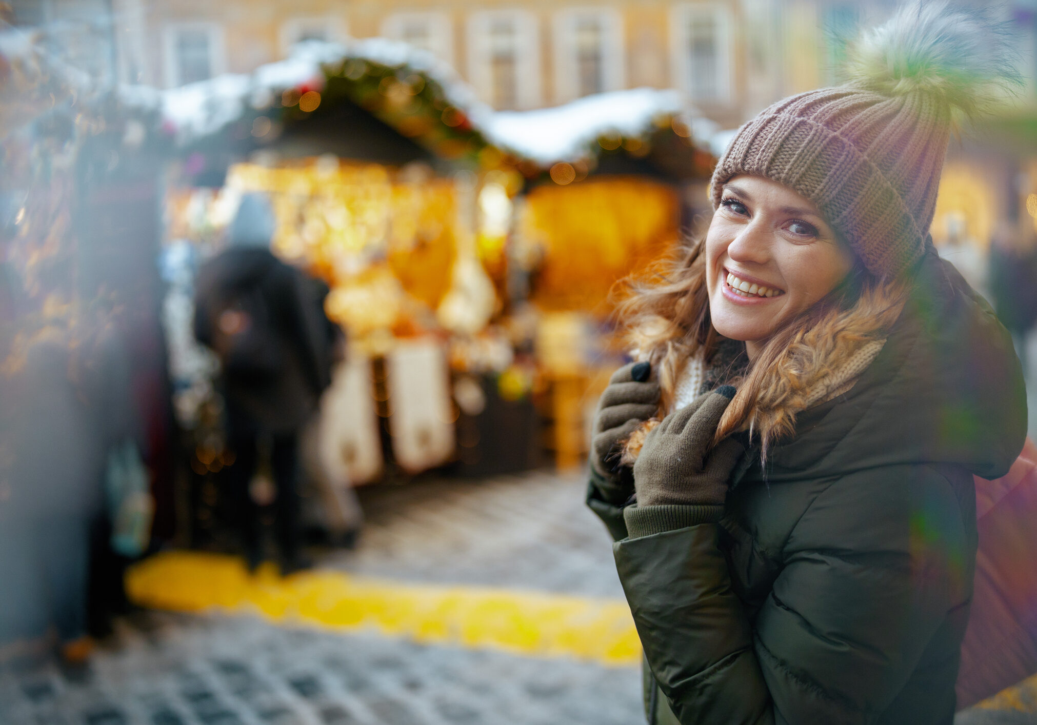 happy modern woman in green coat and brown hat at the christmas fair in the city.