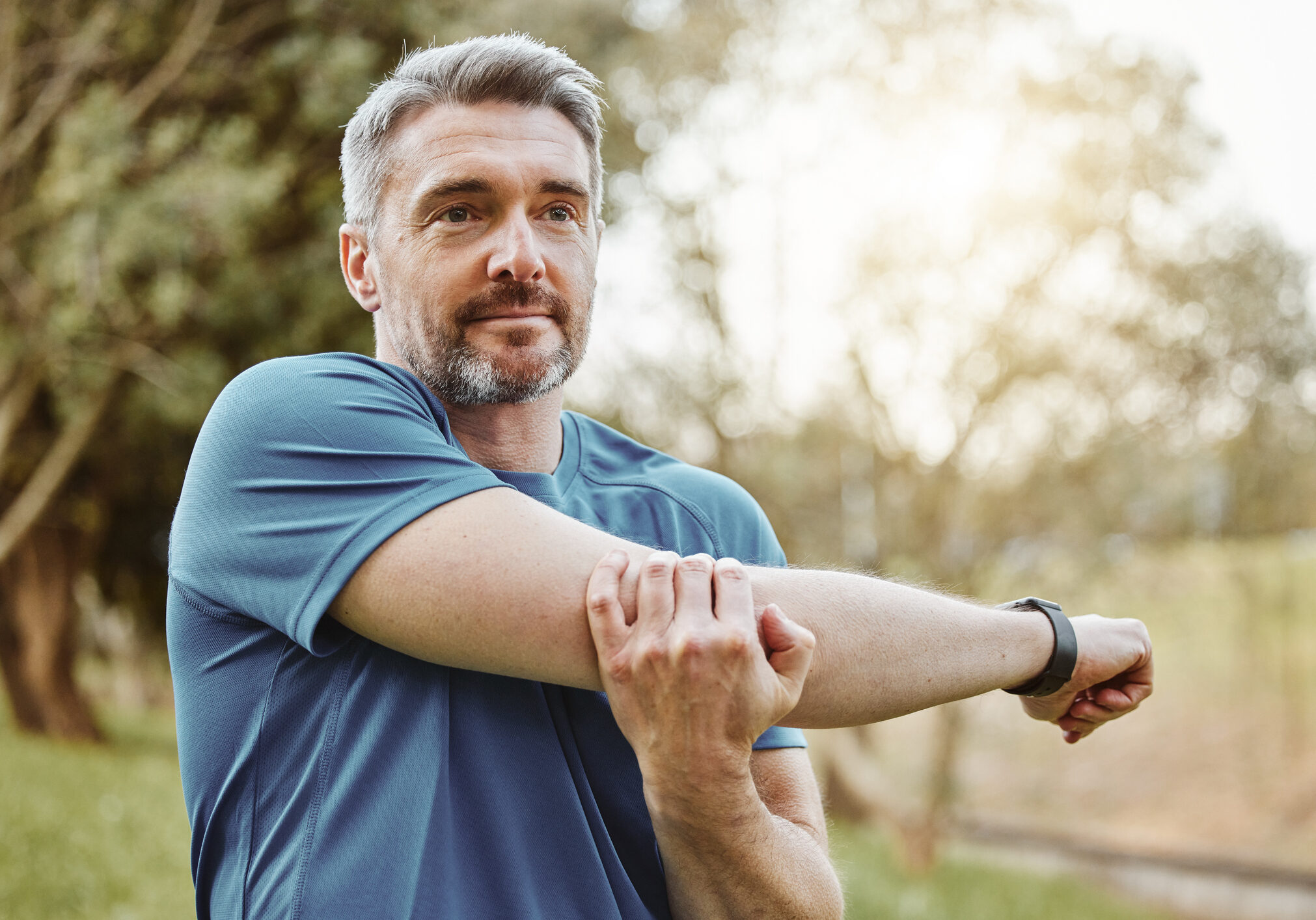 Mature man, arm stretching and outdoor for fitness, wellness and exercise in a park for health. Morning, athlete and training in nature with workout and sports of a calm person ready to start run