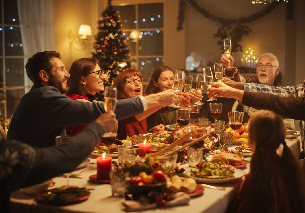 Portrait of a Handsome Young Black Man Proposing a Toast at a Christmas Dinner Table. Family and Friends Sharing Meals, Raising Glasses with Champagne, Toasting, Celebrating a Winter Holiday