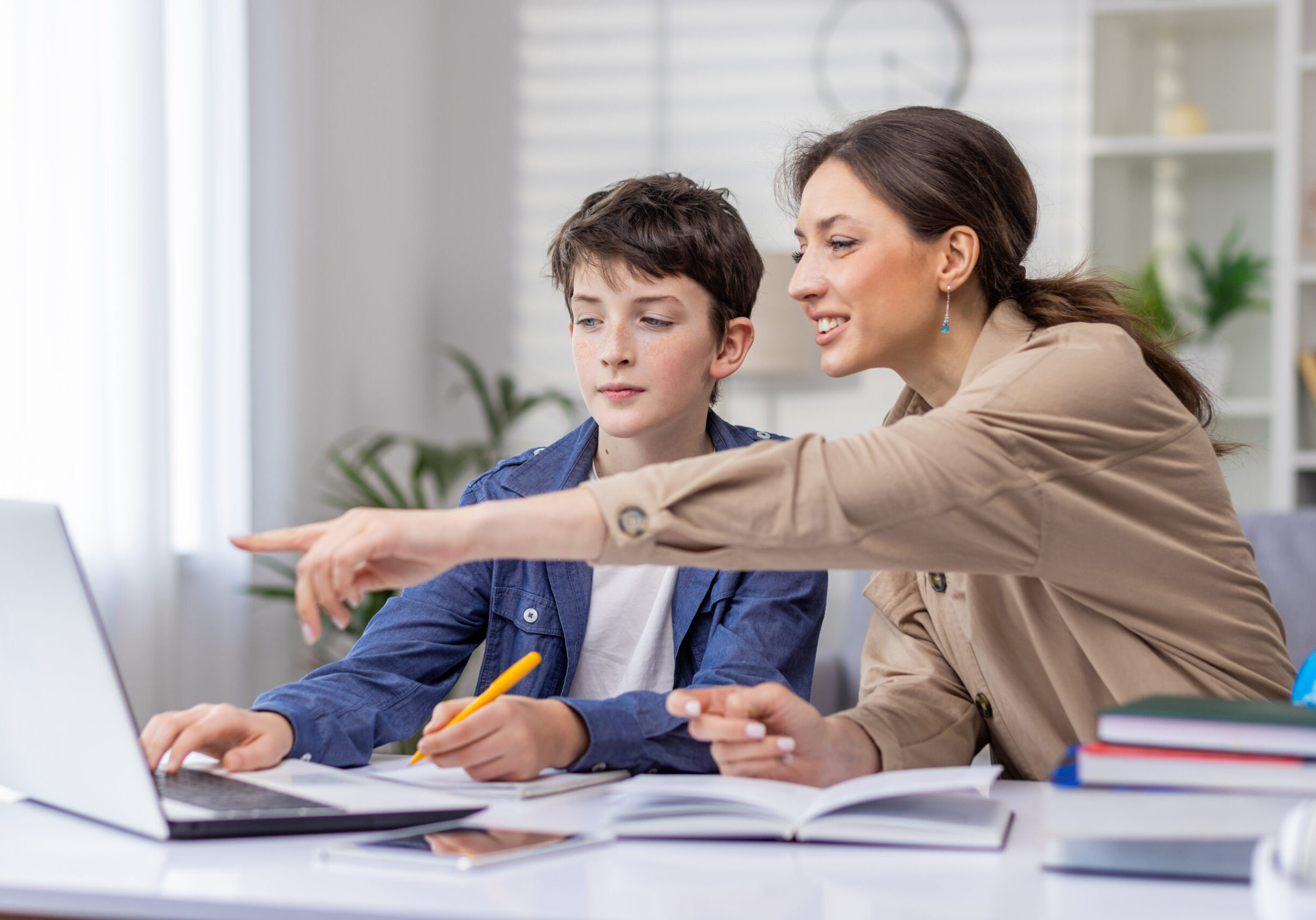 Mother and son studying together sitting at desk at home in living room, boy and woman tutor teaching at home, doing homework together.