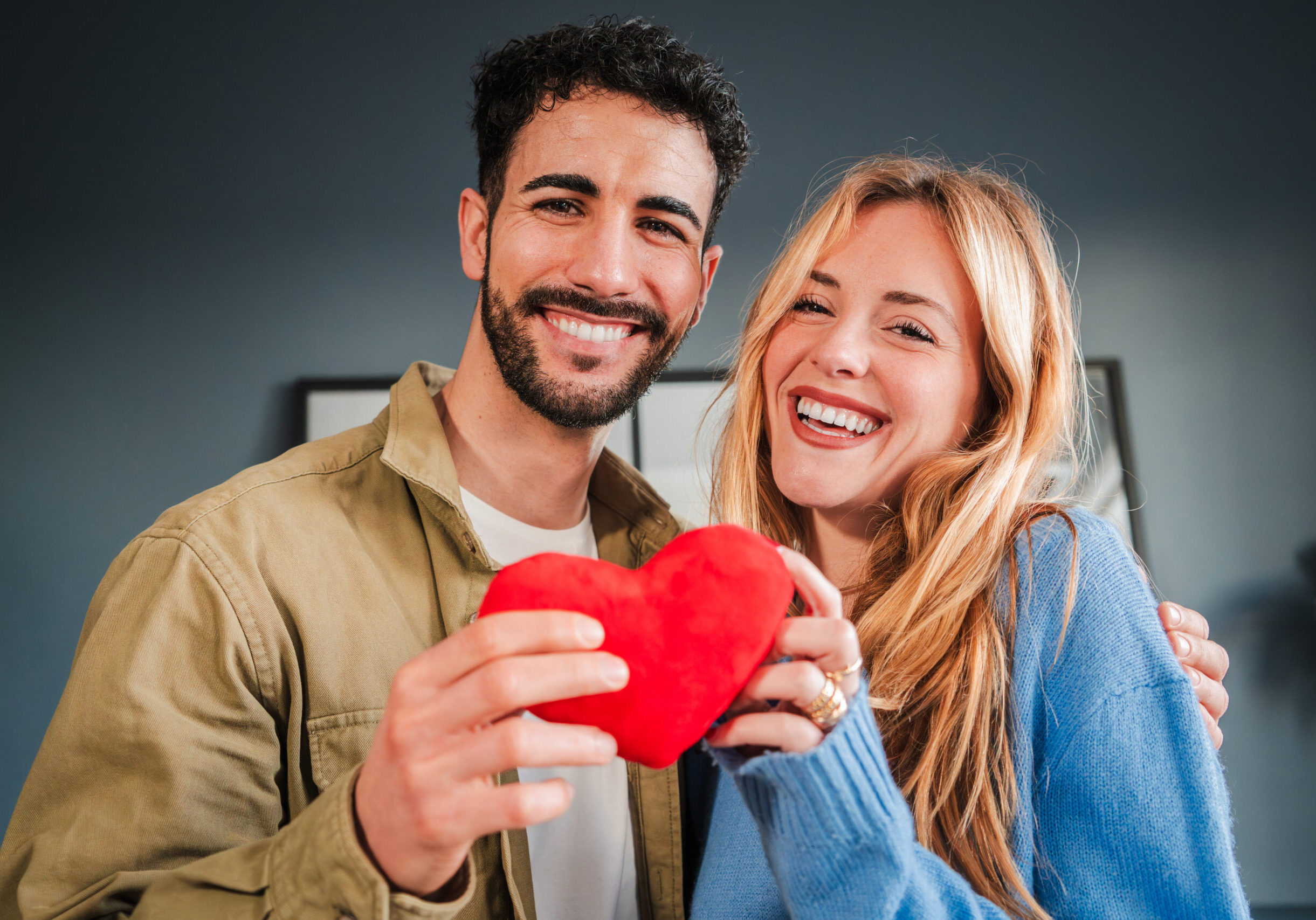Young adorable couple holding a red heart shape smiling and looking at camera with happy expression. Girlfriend and boyfriend celebrating valentines day festivity or relationship anniversary together. High quality photo